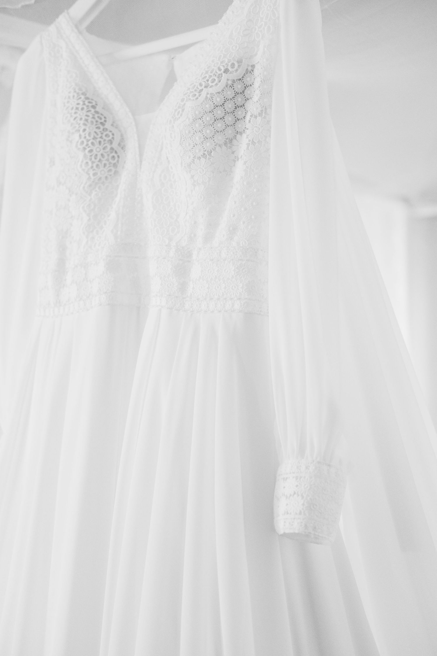 Close-up details of delicate white lace wedding dresses hanging in a row.