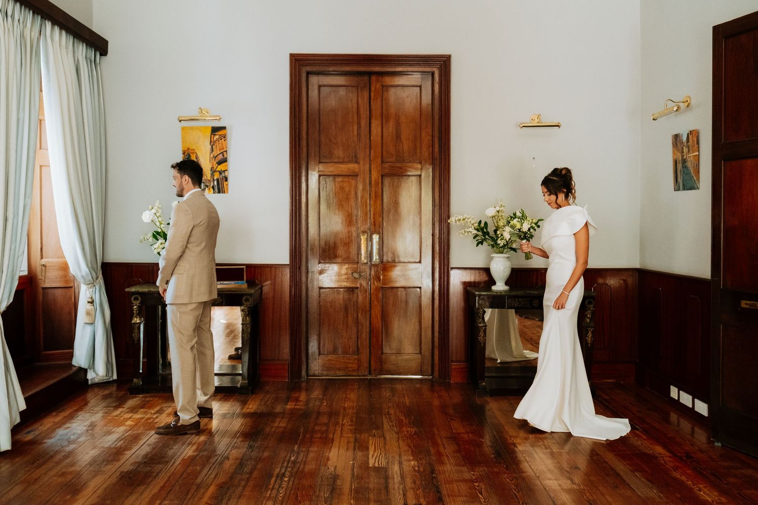 Groom in beige and bride in white suit in their first lok at Gibraltar City Hall