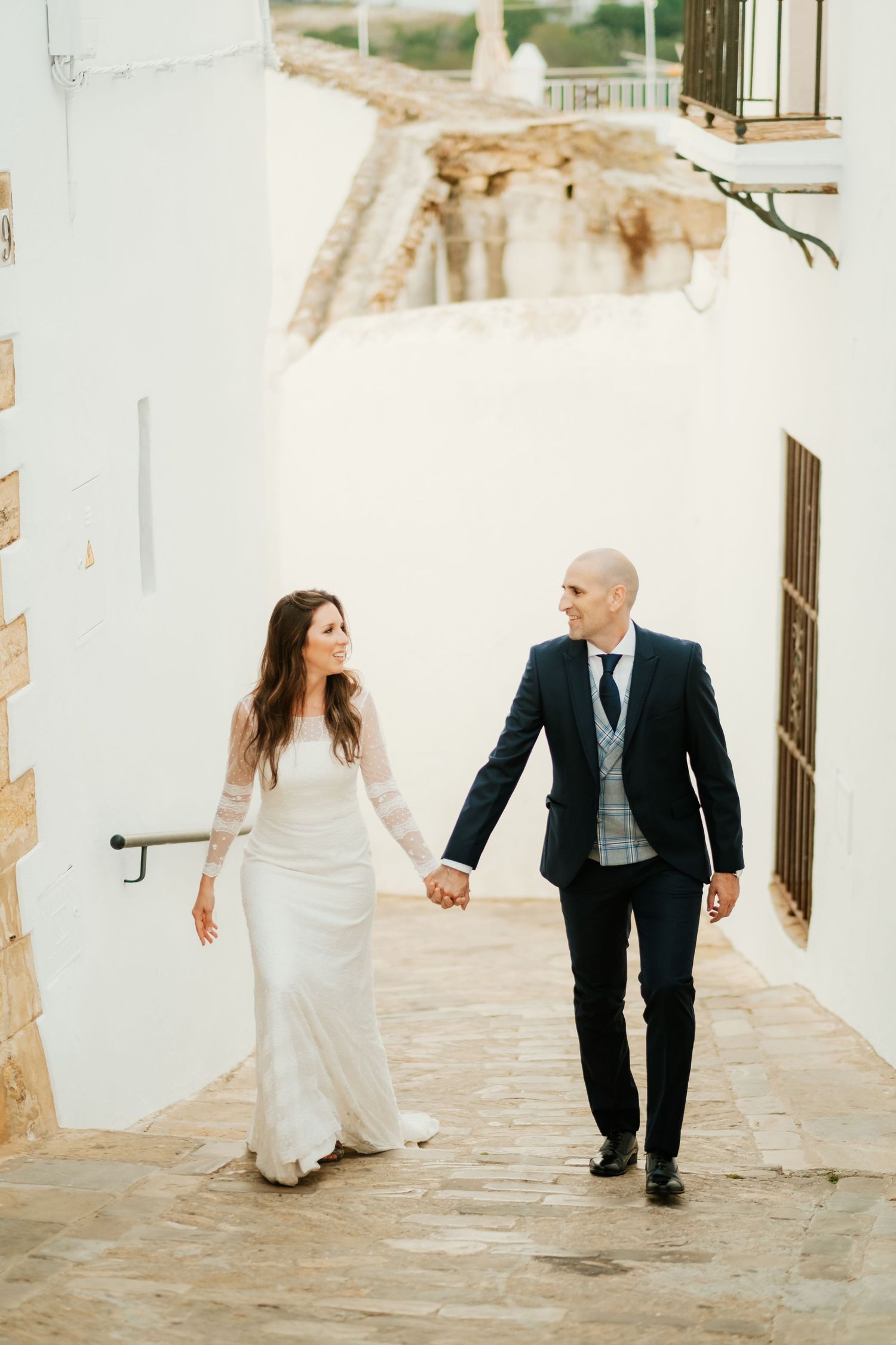 Novios caminando bajo los contrafuertes y arcos blancos de Vejer al atardecer