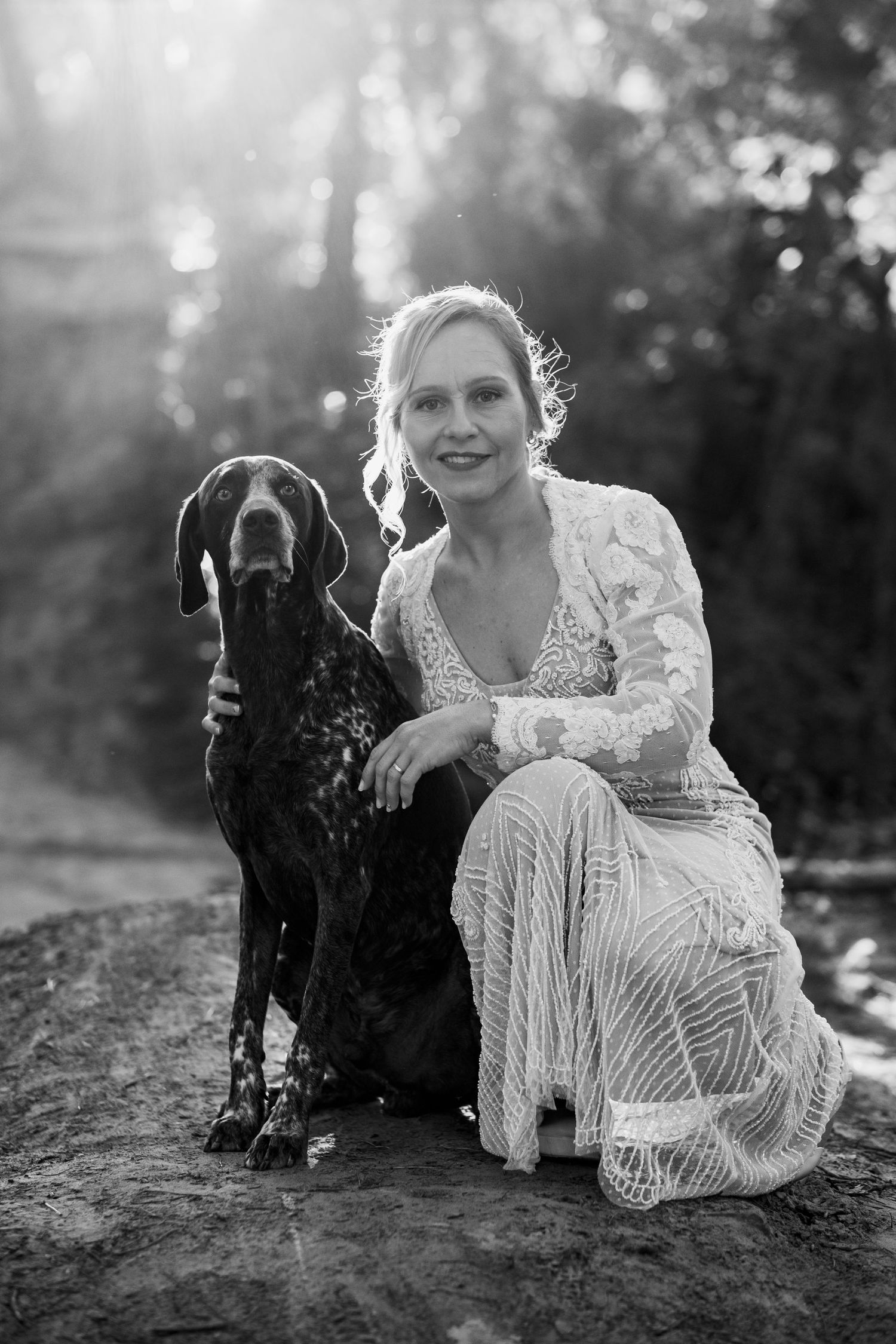 Retrato vertical en blanco y negro de Alejandra con su perro bajo la luz única del Pinar del Rey