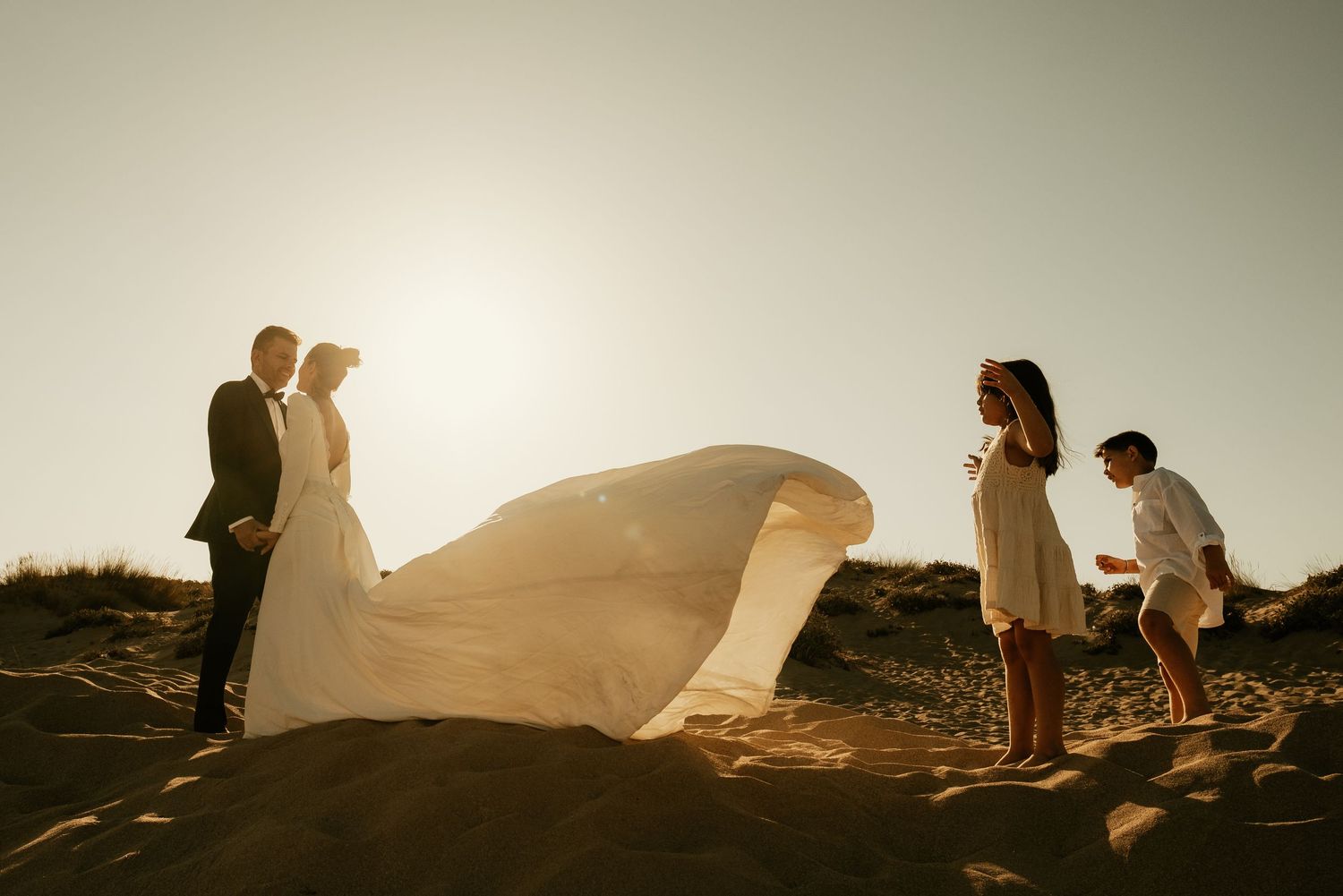 Contraluz documental de pareja con María y Lucas jugando con la cola del vestido Sajorami Beach Laura y Fernando Roberto Pecino