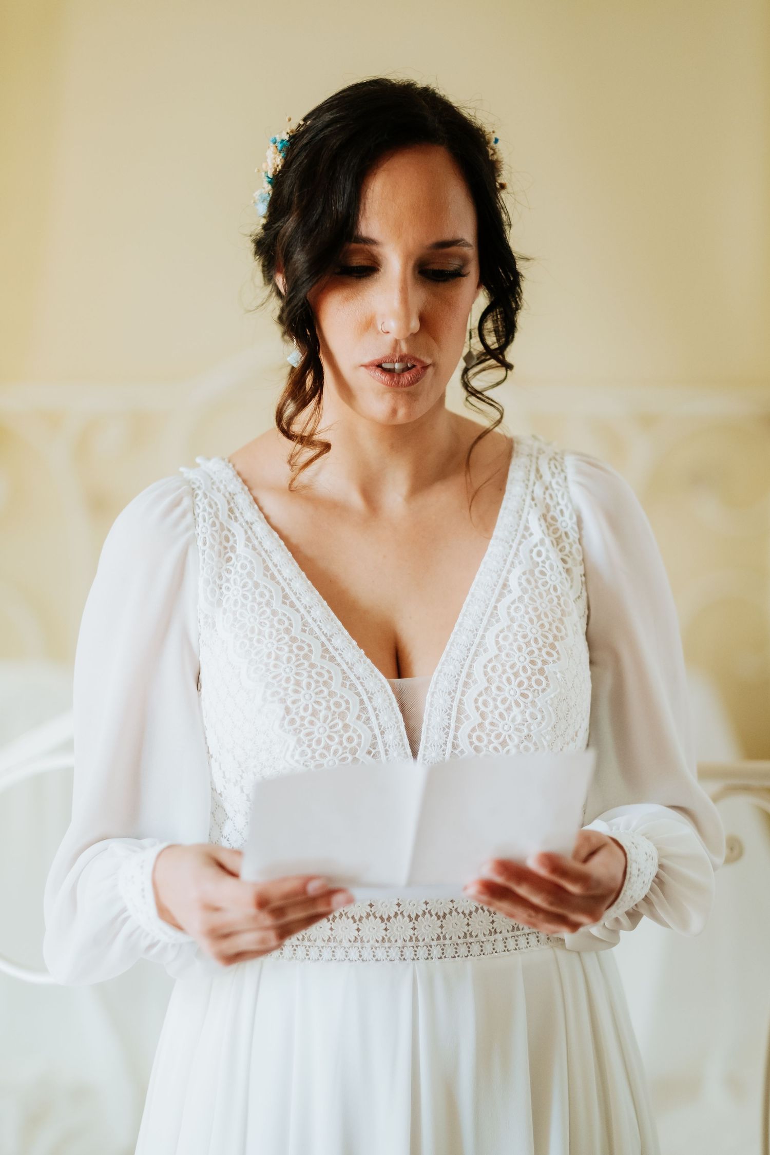 A bride in a vintage-inspired white lace dress reads letters while getting ready on her wedding day.