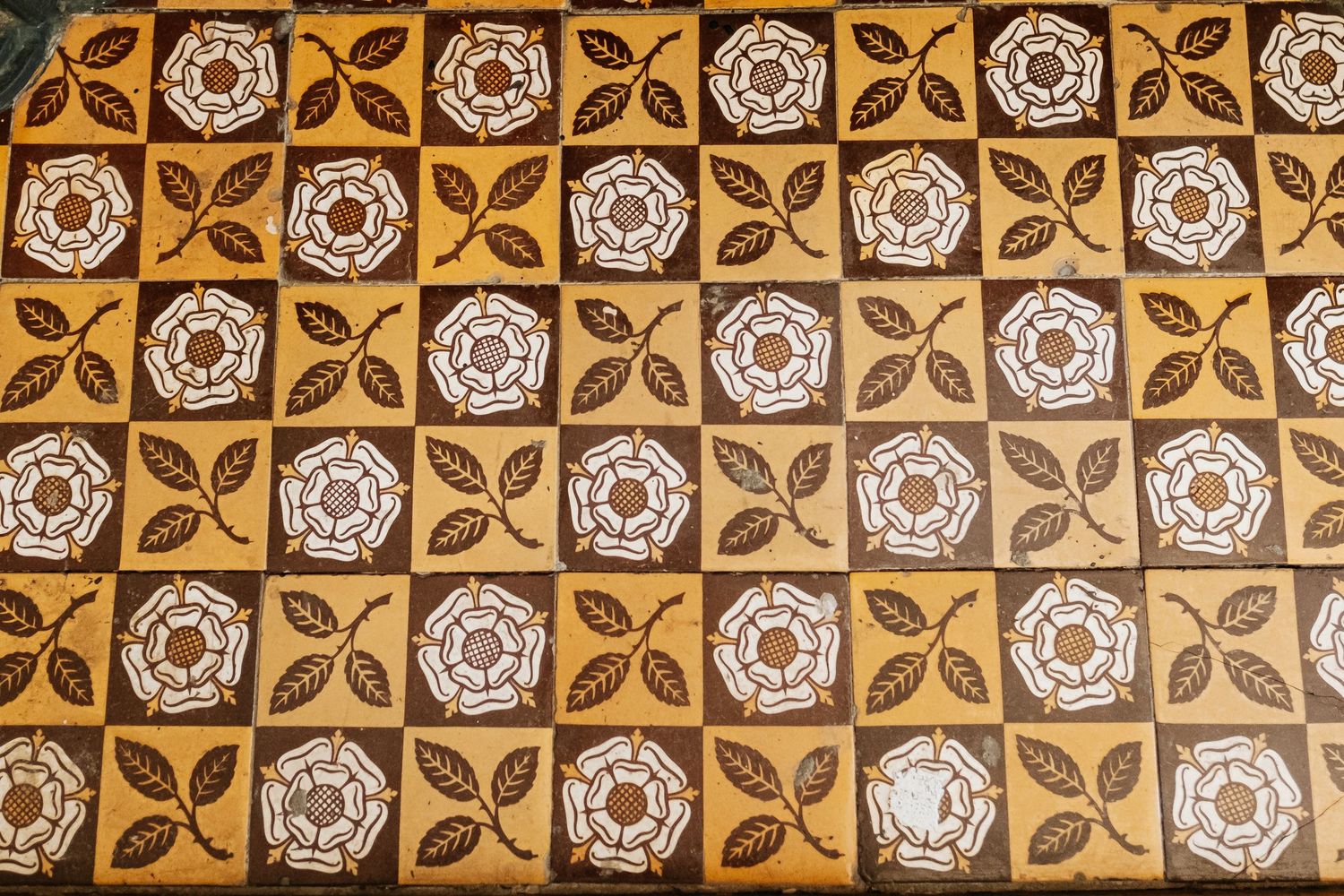 Decorative vintage tile pattern with alternating gold and white floral motifs in a repeating design. Gibraltar Heritage