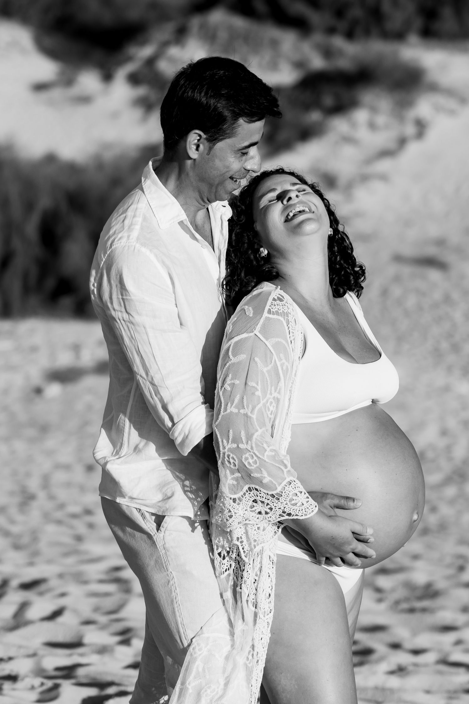 A couple shares a romantic moment on the beach in black and white as they celebrate an expected arrival.