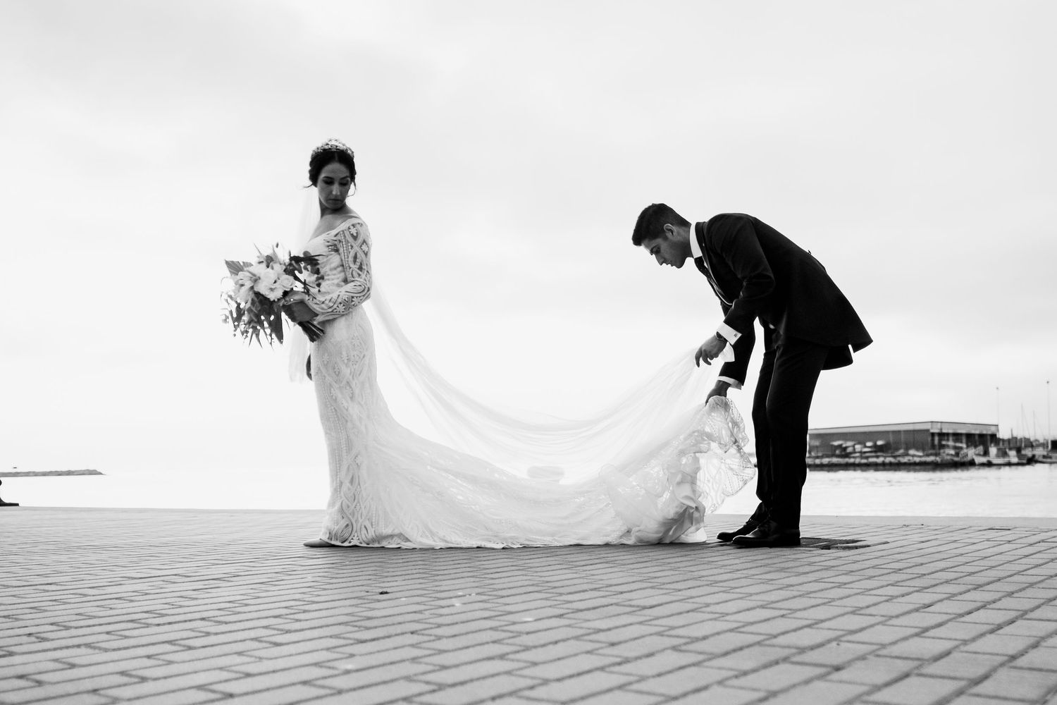 Fotografía de boda en blanco y negro, el novio cuidando los detalles del vestido de la novia