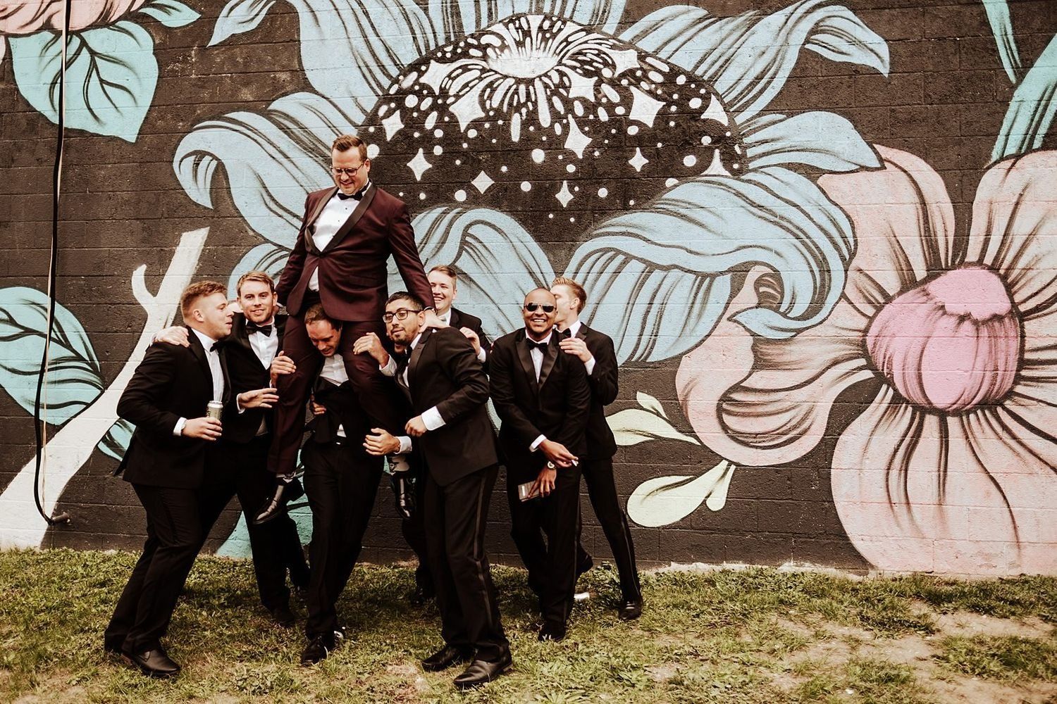 Groomsmen tossing Karel into the air in front of a colorful graffiti wall in downtown Grand Rapids.