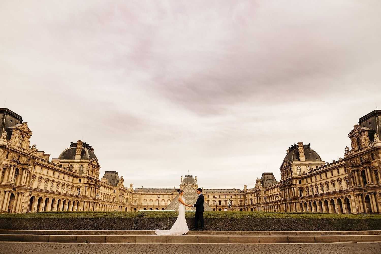 marisa y cristian compartiendo una mirada complice frente a la piramide del museo del louvre en paris