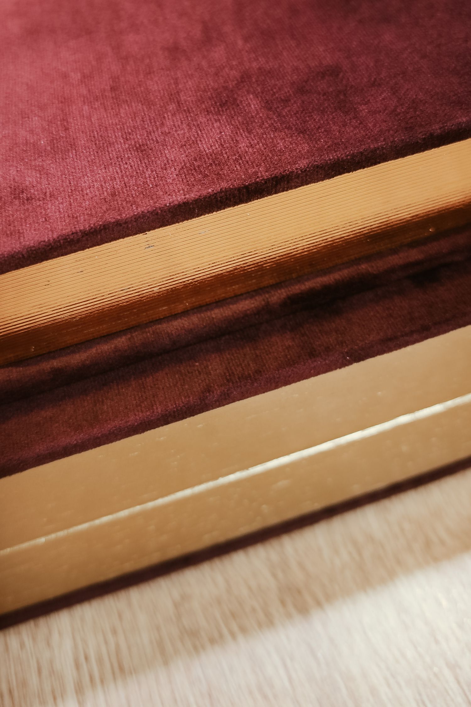 Close-up macro photography showing segments of a burgundy velvet fabric against a beige wooden surface or trim.
