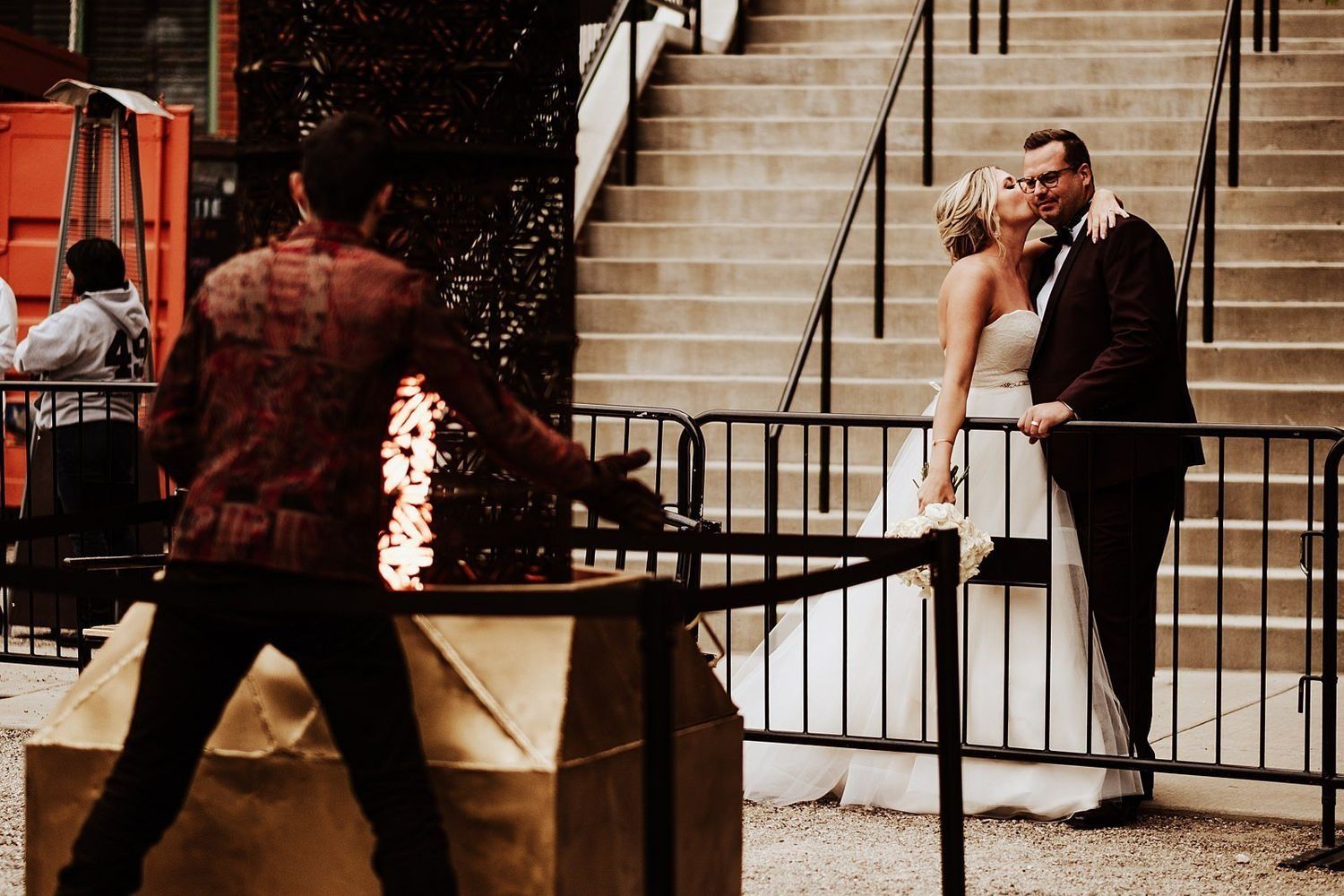 wedding kiss with a street fire performer in the background in Grand Rapids