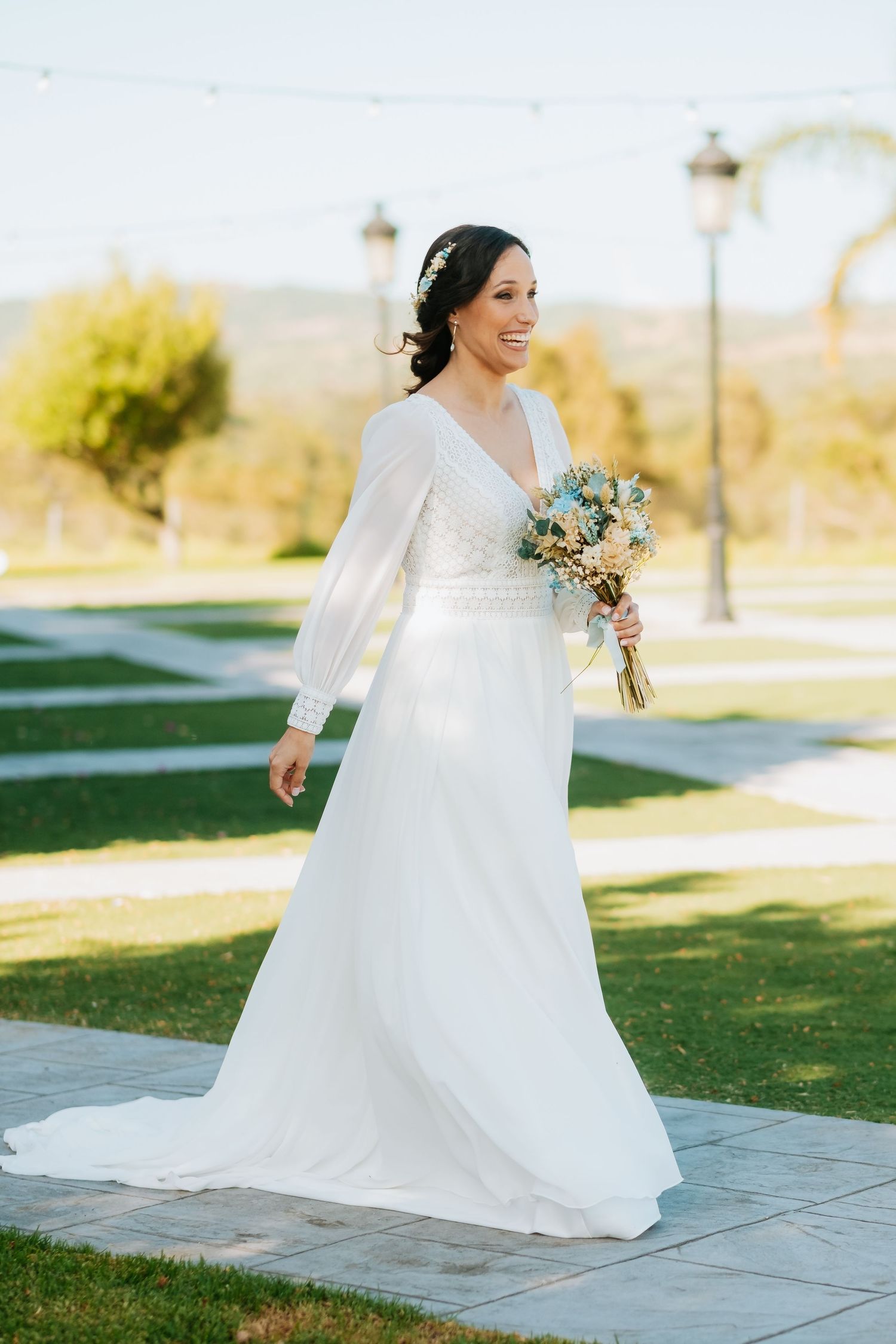 Bride in flowing white wedding dress twirling outdoors on stone patio.
