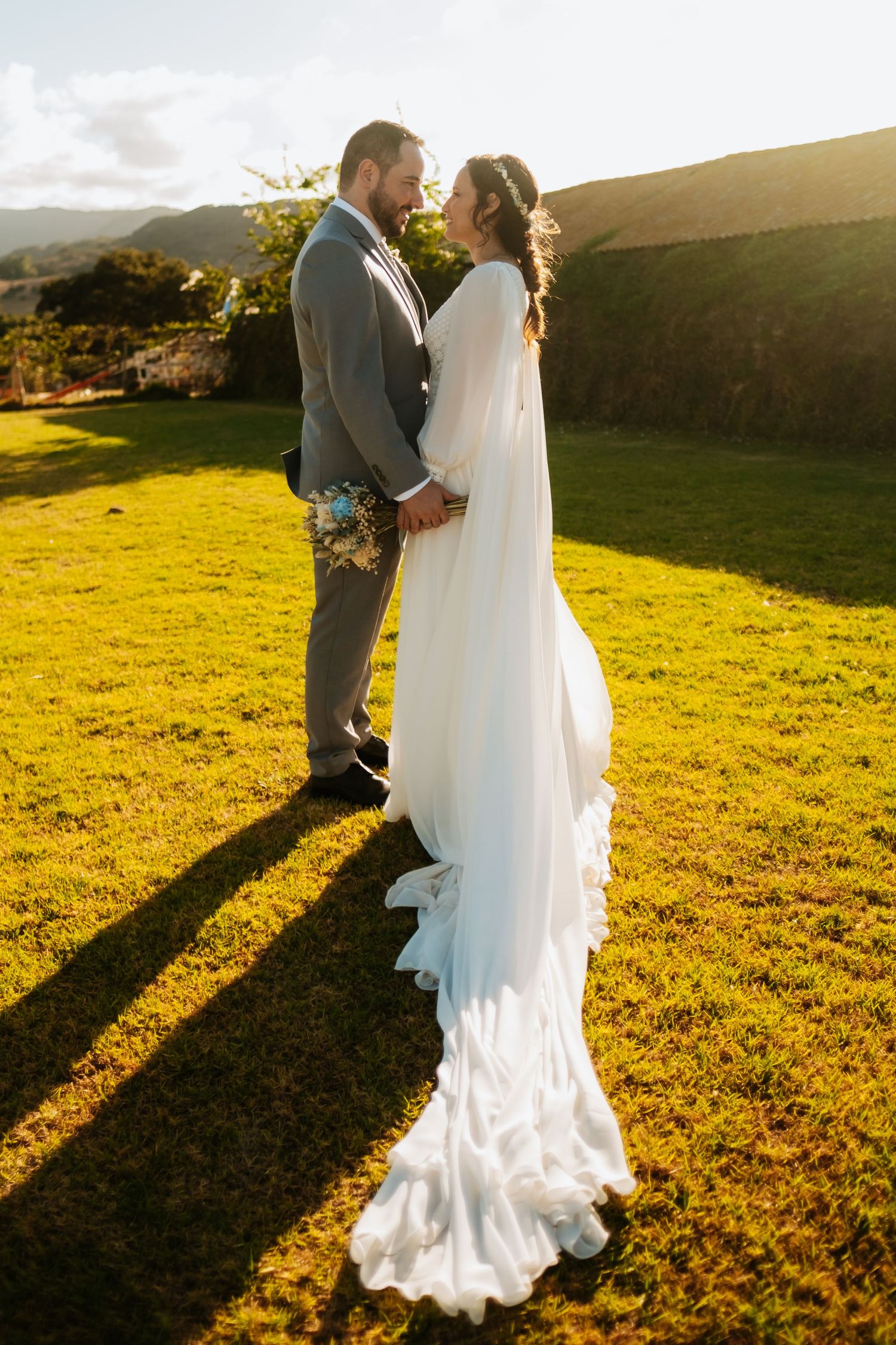 Wedding couple poses in golden sunset light on a grassy hillside.