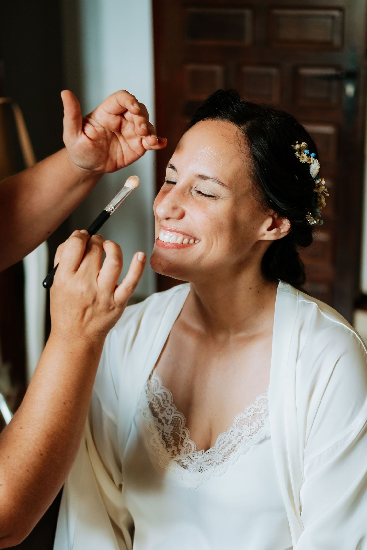 Someone in a white robe getting makeup applied during wedding preparations.