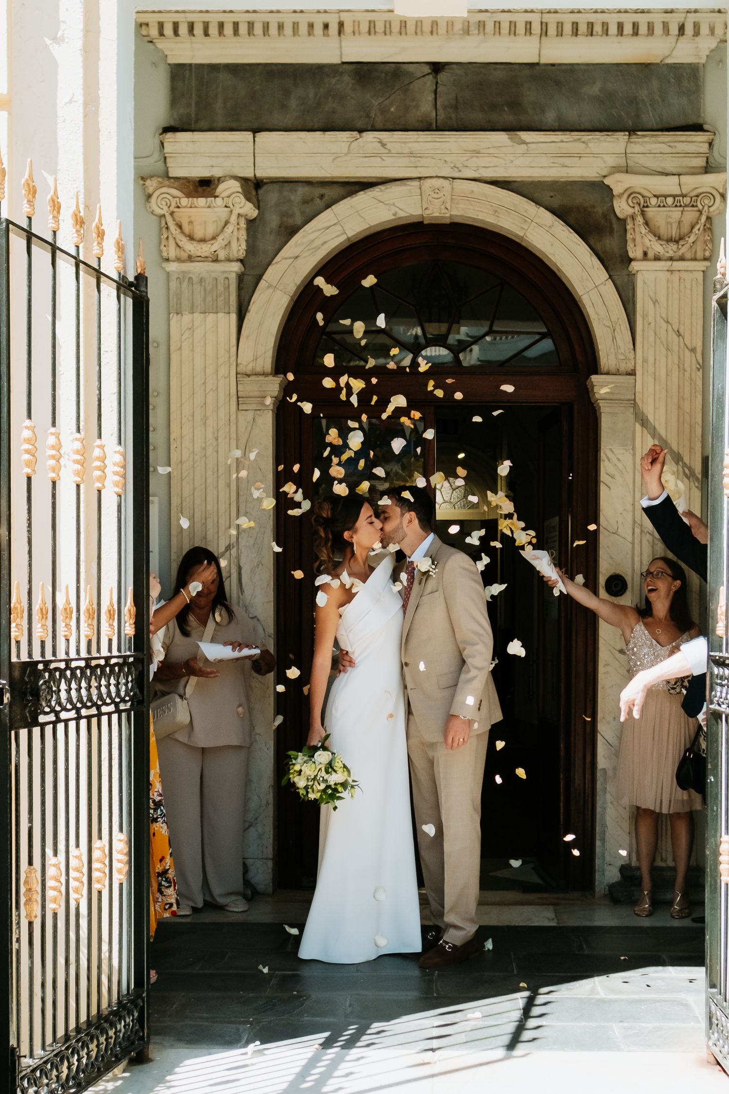 Wedding celebration with flower petals being tossed in front of ornate stone archway.