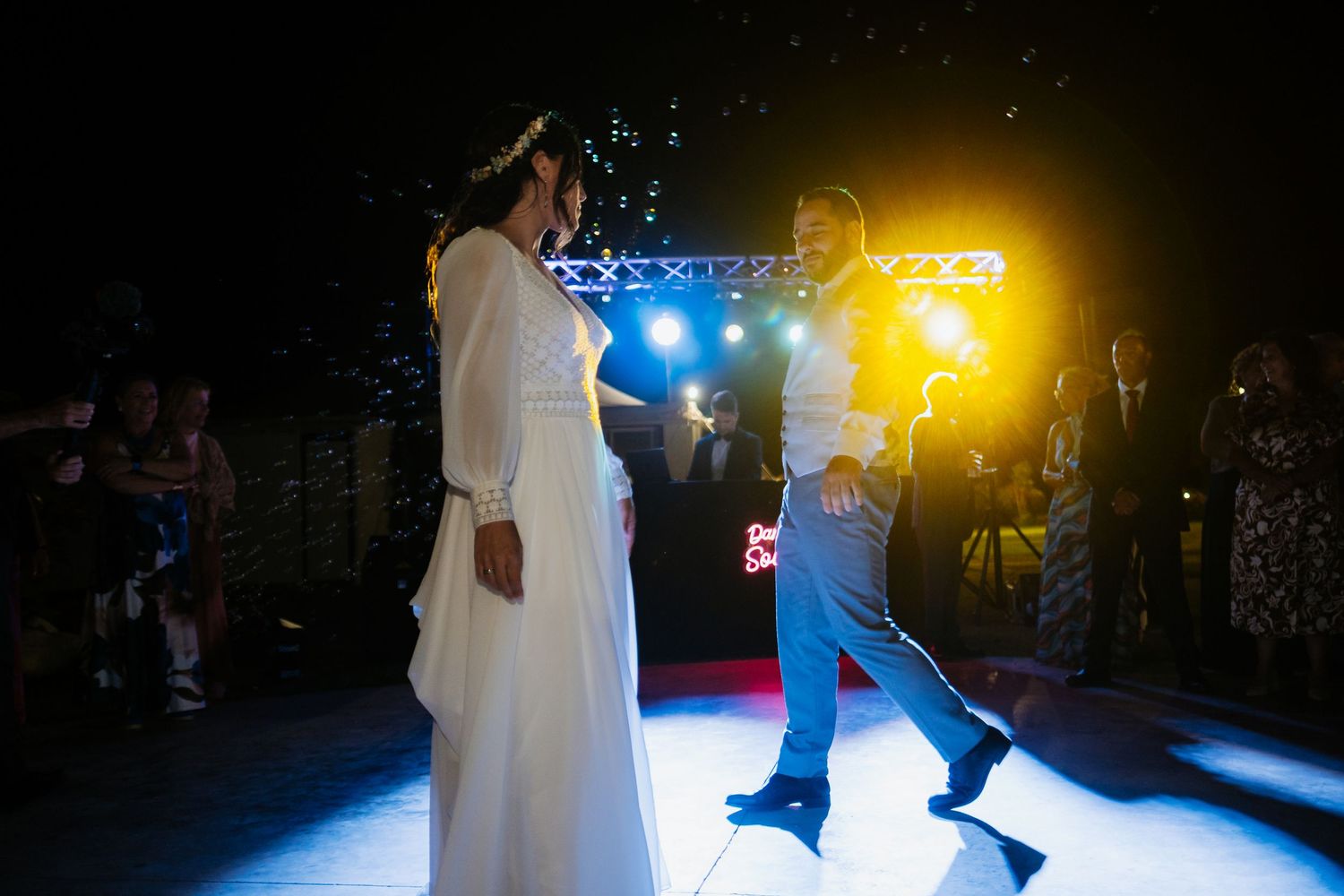 Wedding party dancing under colorful stage lights at an evening reception.