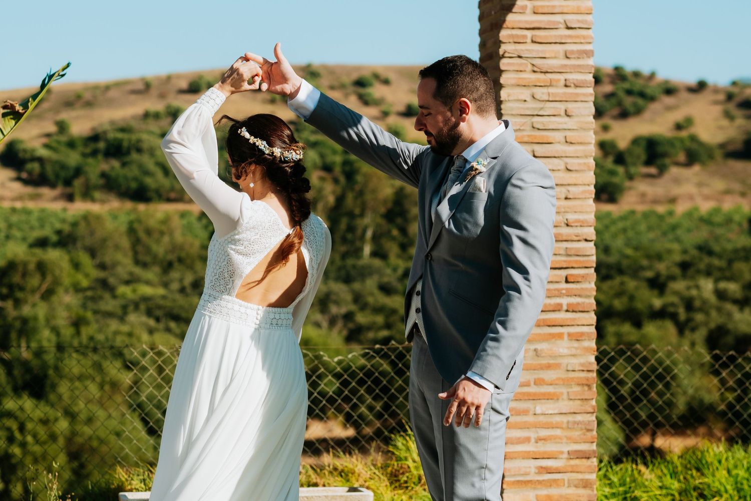 Couple dancing and celebrating together outdoors against brick wall and natural landscape.