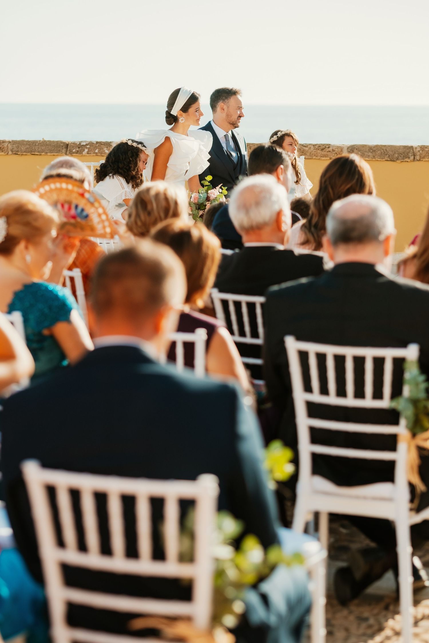 Perspectiva desde atrás de los invitados mirando al mar y novios