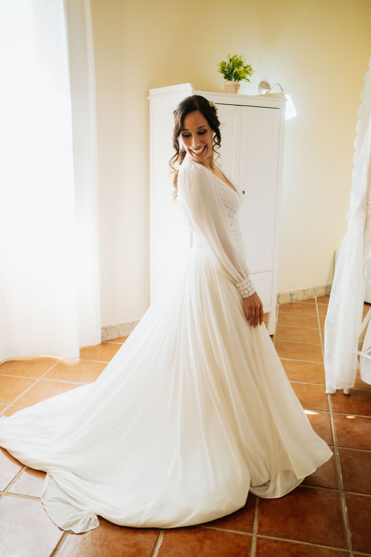 Elegant white wedding dress with long sleeves twirls on terracotta tile flooring.