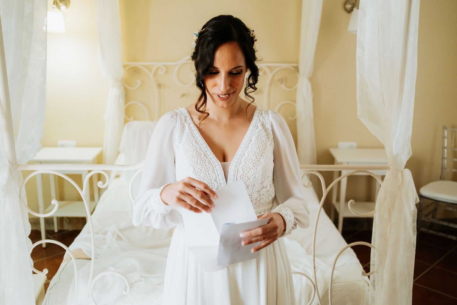 Bride in a white gown gets ready in an elegant room with vintage furniture and natural lighting.