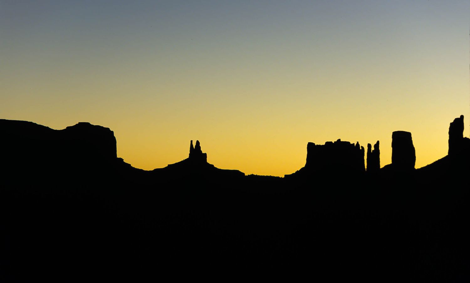 Sunrise over Monument Valley silhouettes stand against a glowing yellow dusk sky, creating a bold Southwest horizon scene.