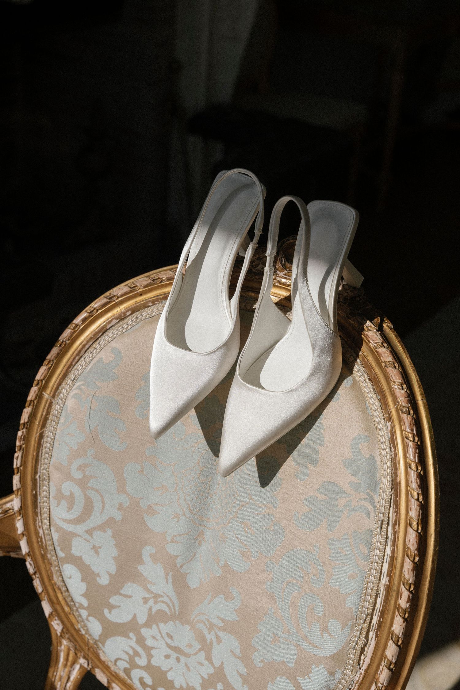 White bridal shoes arranged in a heart shape on an elegant vintage-style damask patterned tray with gold trim.