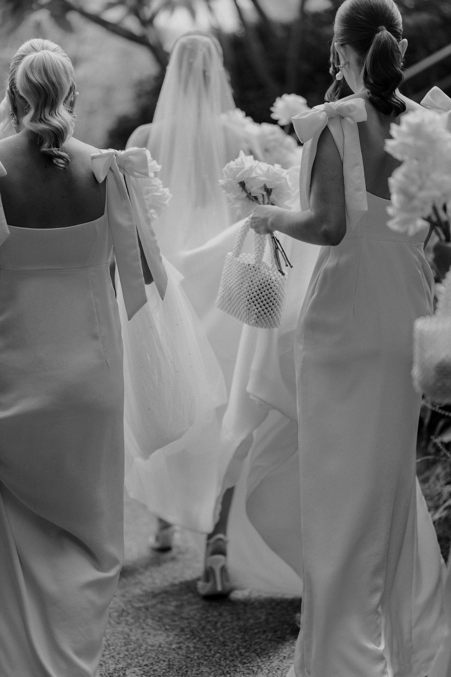 Artistic black and white shot of bridesmaids walking with the bride through a garden setting.