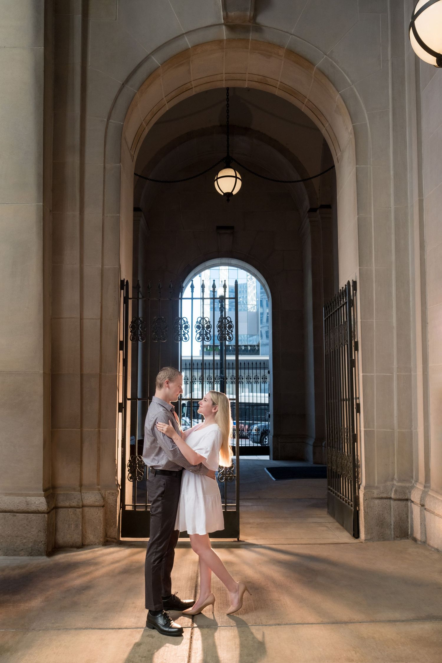 A couple shares a romantic moment beneath an elegant arched passageway with ornate architectural details and ambient lighting.