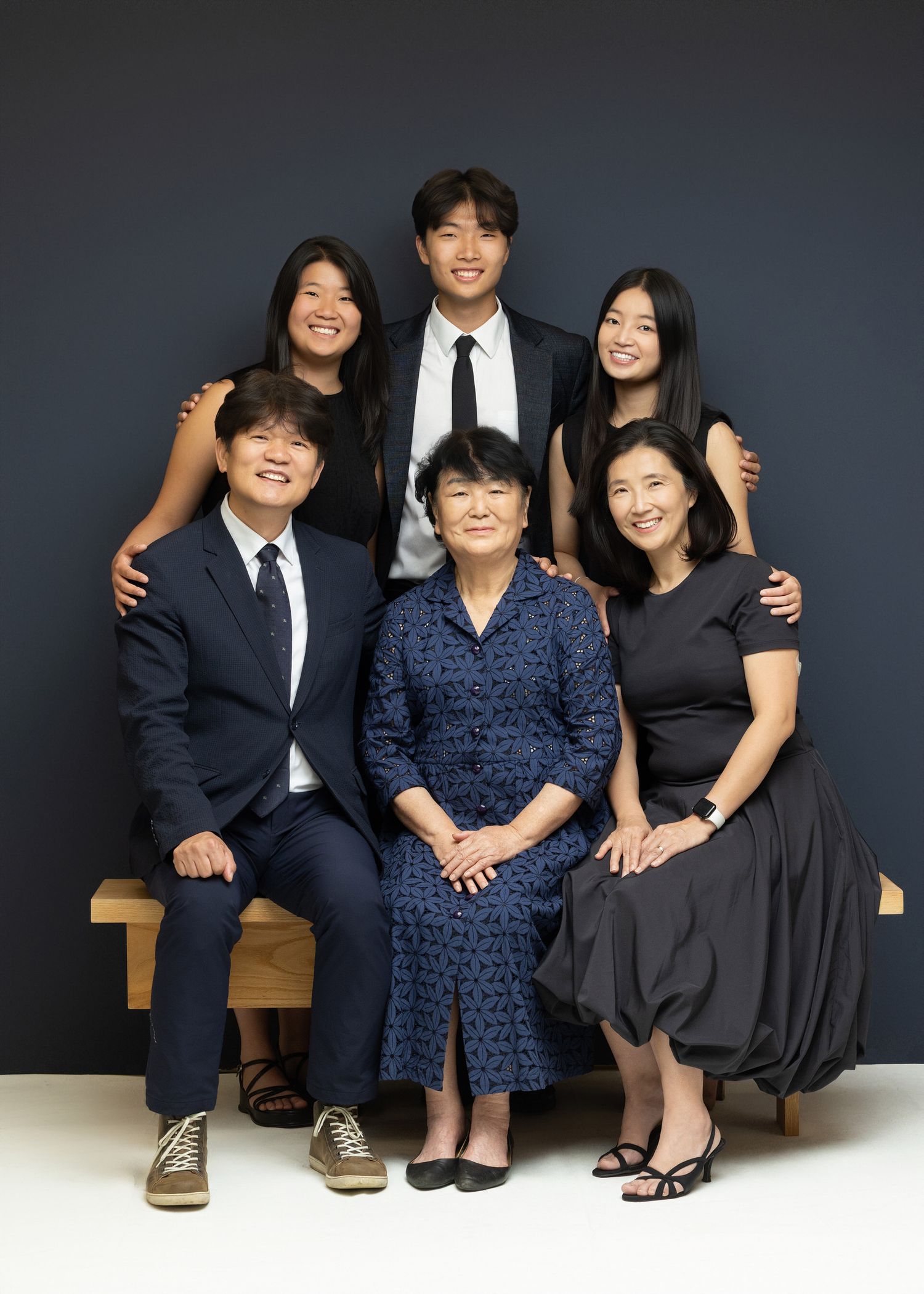 Three people in formal attire pose together for a series of studio portraits against a dark background.
