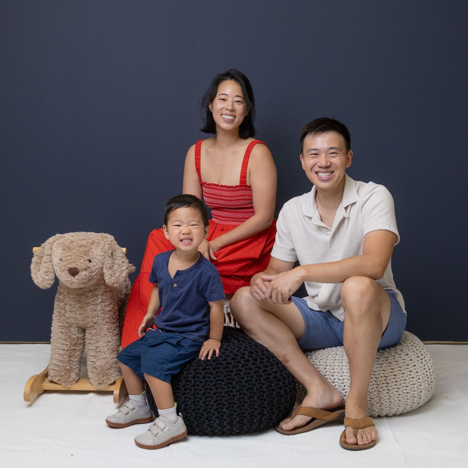 Family sitting together on white floor with plush teddy bear, captured in casual studio setting.