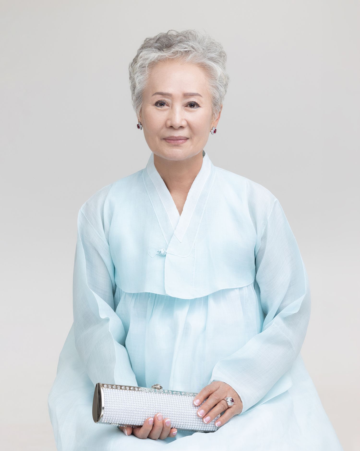 A person in a light blue traditional Korean hanbok dress sits gracefully against a white studio background.
