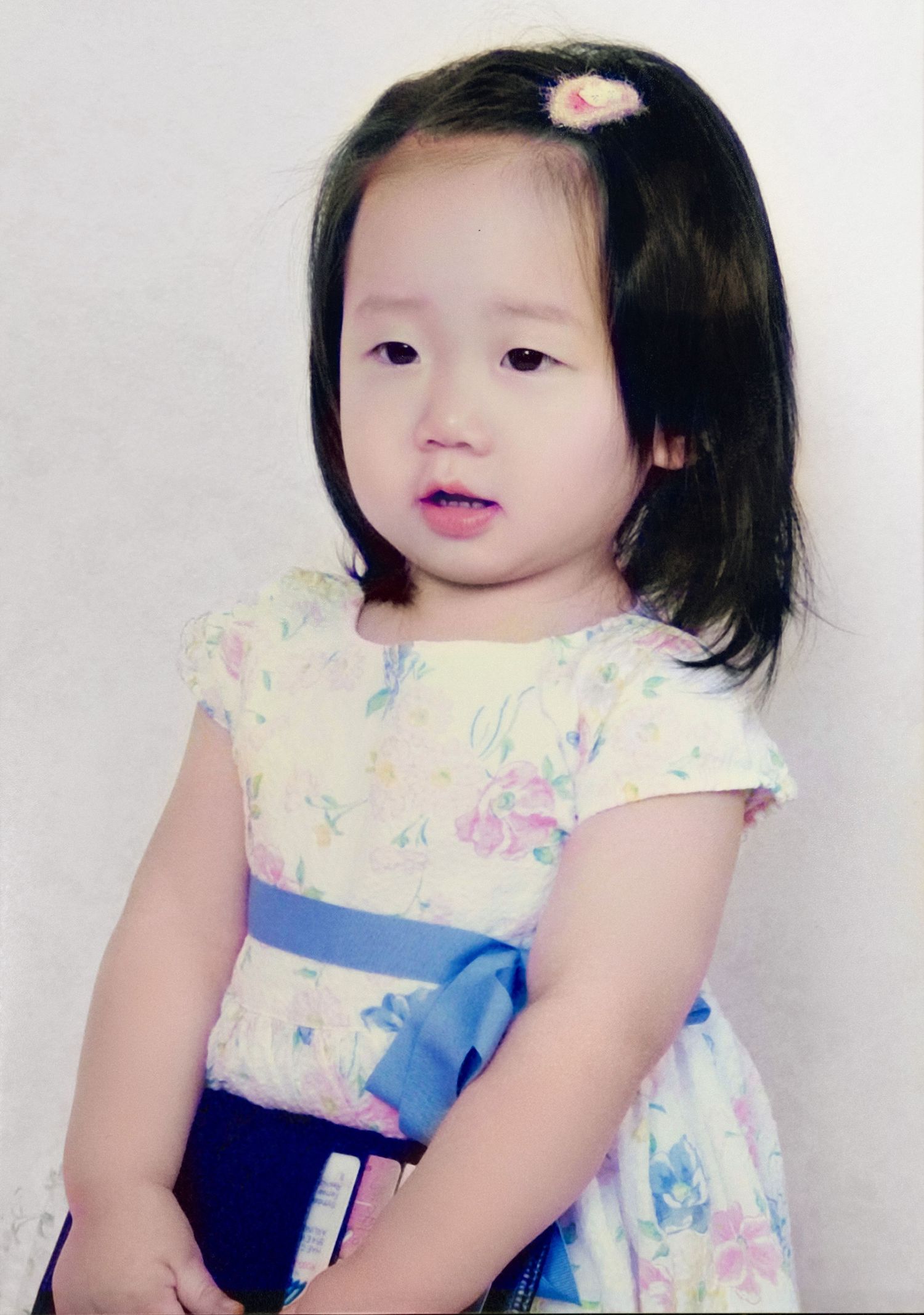 A toddler in a floral dress with a blue sash poses for four sequential portrait photos against a white background.