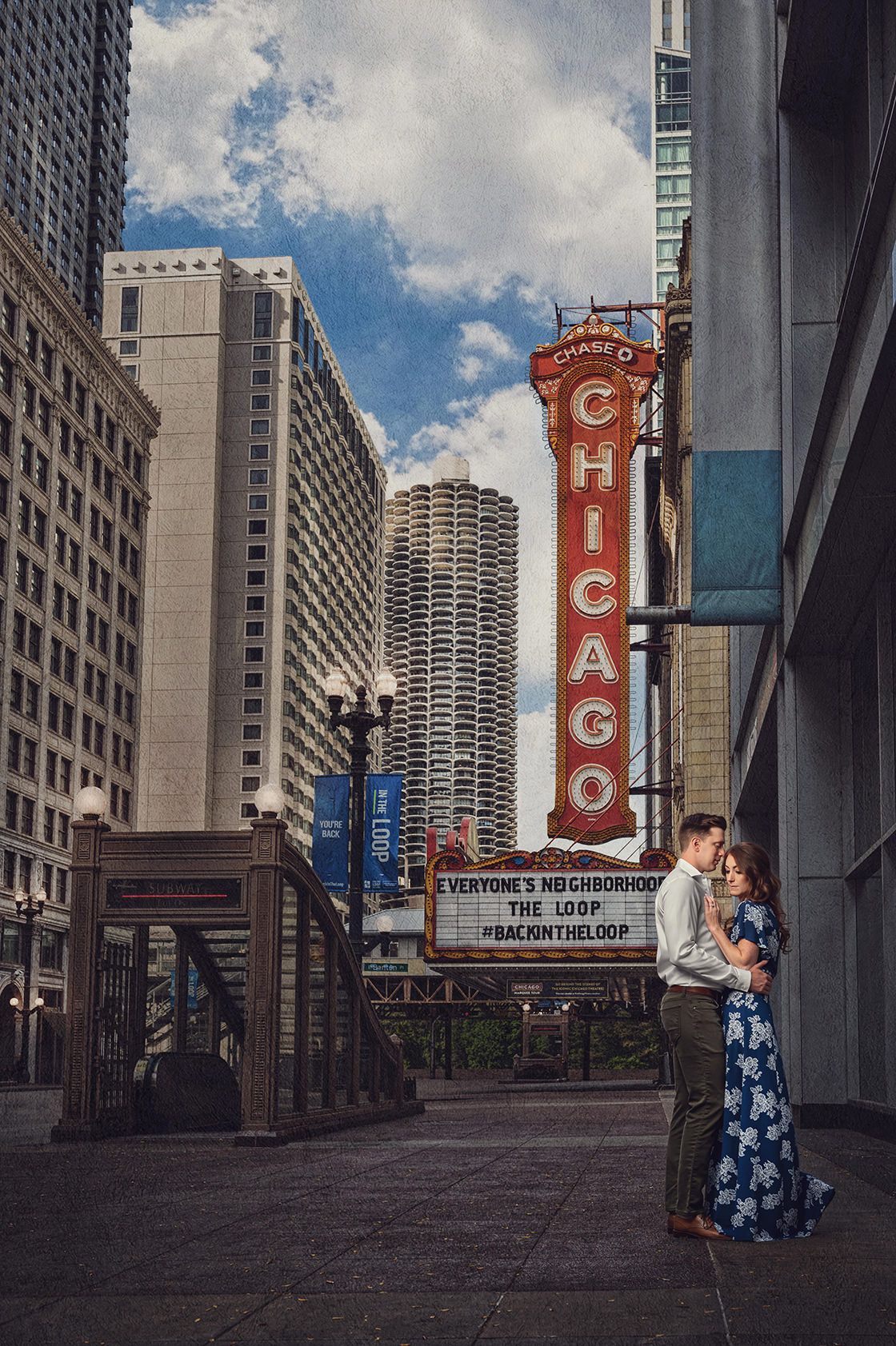 Couple embracing in front of iconic Chicago Theatre sign on State Street with city skyline in background.