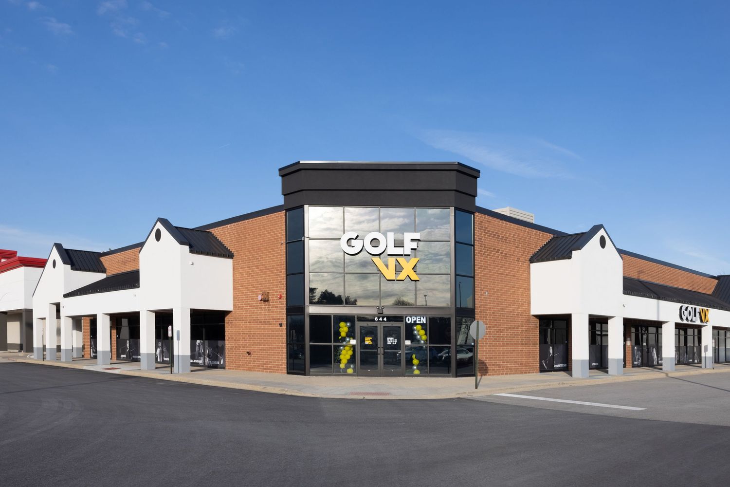 Modern retail strip mall with brick facade and large storefront windows under bright blue sky.