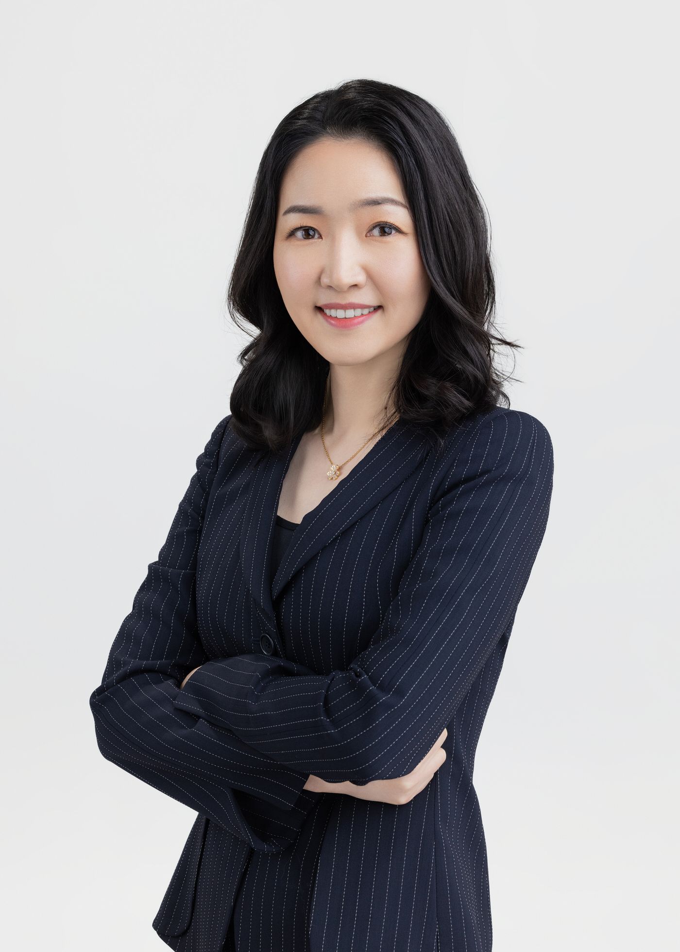 Professional wearing a navy pinstriped blazer poses with crossed arms in a studio setting.