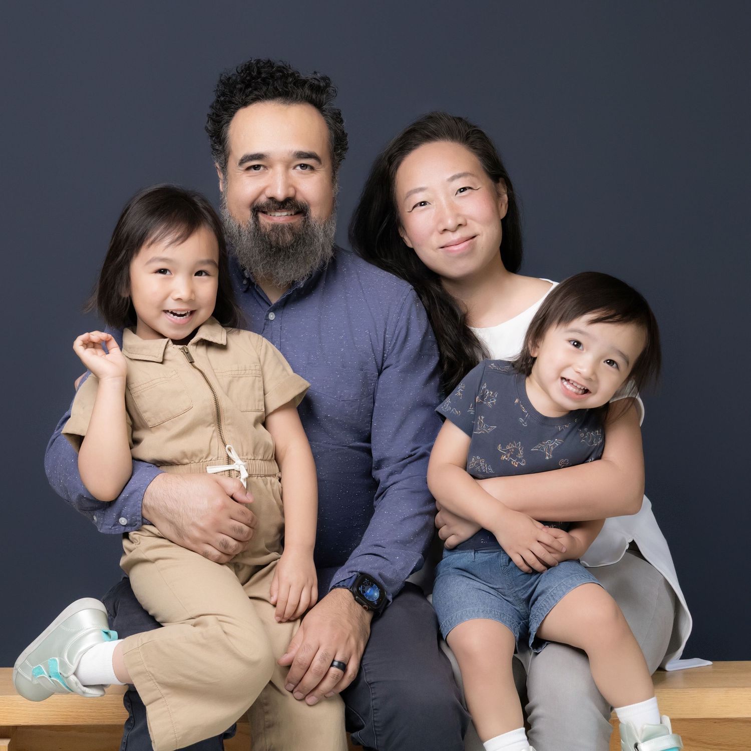 A happy family of four poses for a professional portrait against a dark blue background in a photography studio.