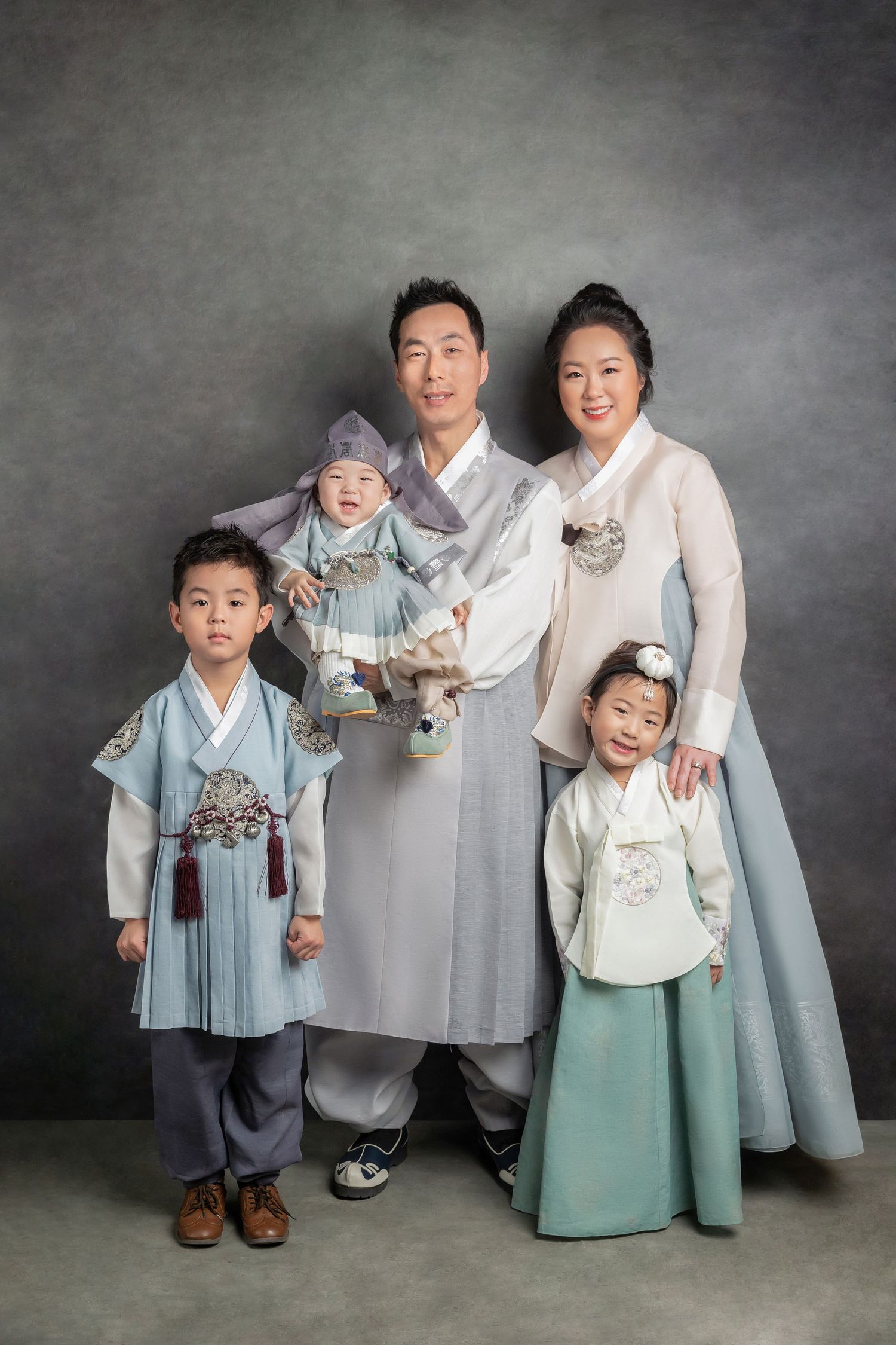Korean family poses in traditional hanbok attire for a heartwarming photo shoot across four mood-lit portraits.