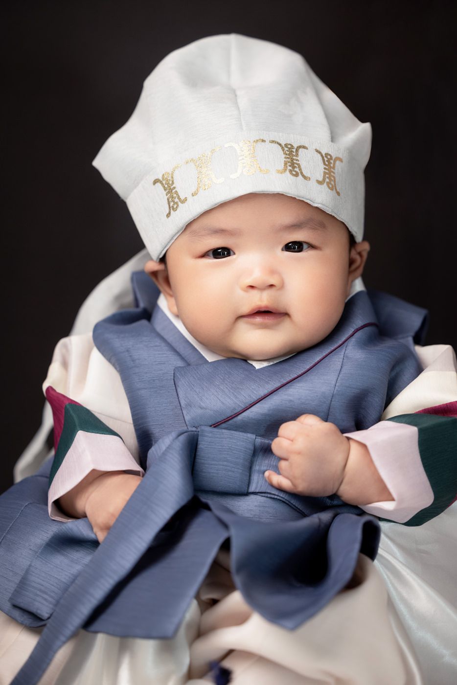 A baby wearing a white cap and navy blue outfit smiles in a series of progressive close-up photos against a black background.
