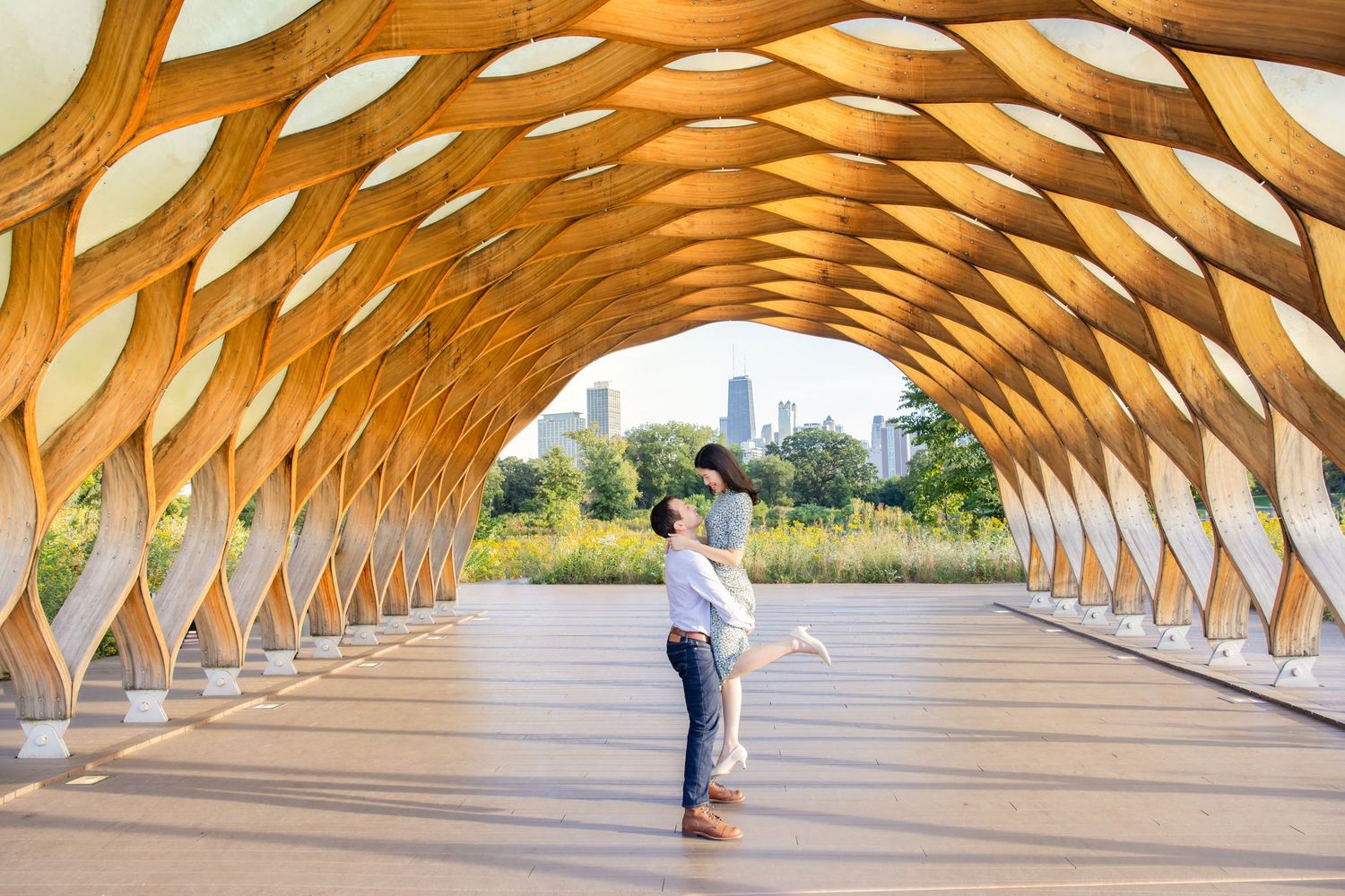 A wooden curved architectural walkway with repeating arched beams creates a striking geometric pattern in an outdoor setting.