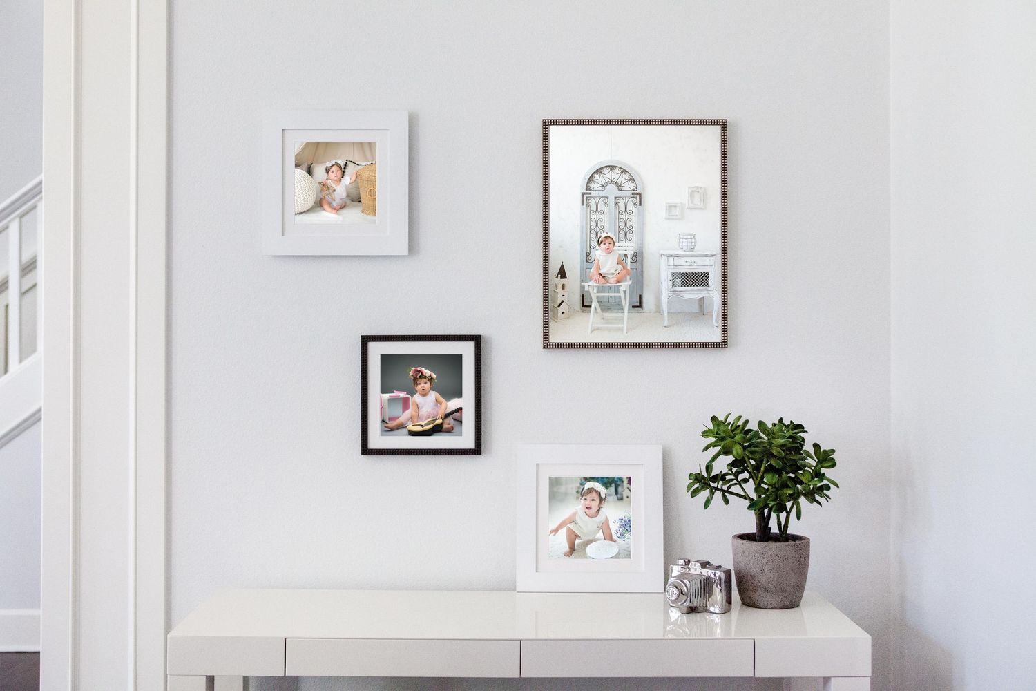 Gallery wall display of framed artwork and photos above a white table with a potted plant in a bright, minimalist room.