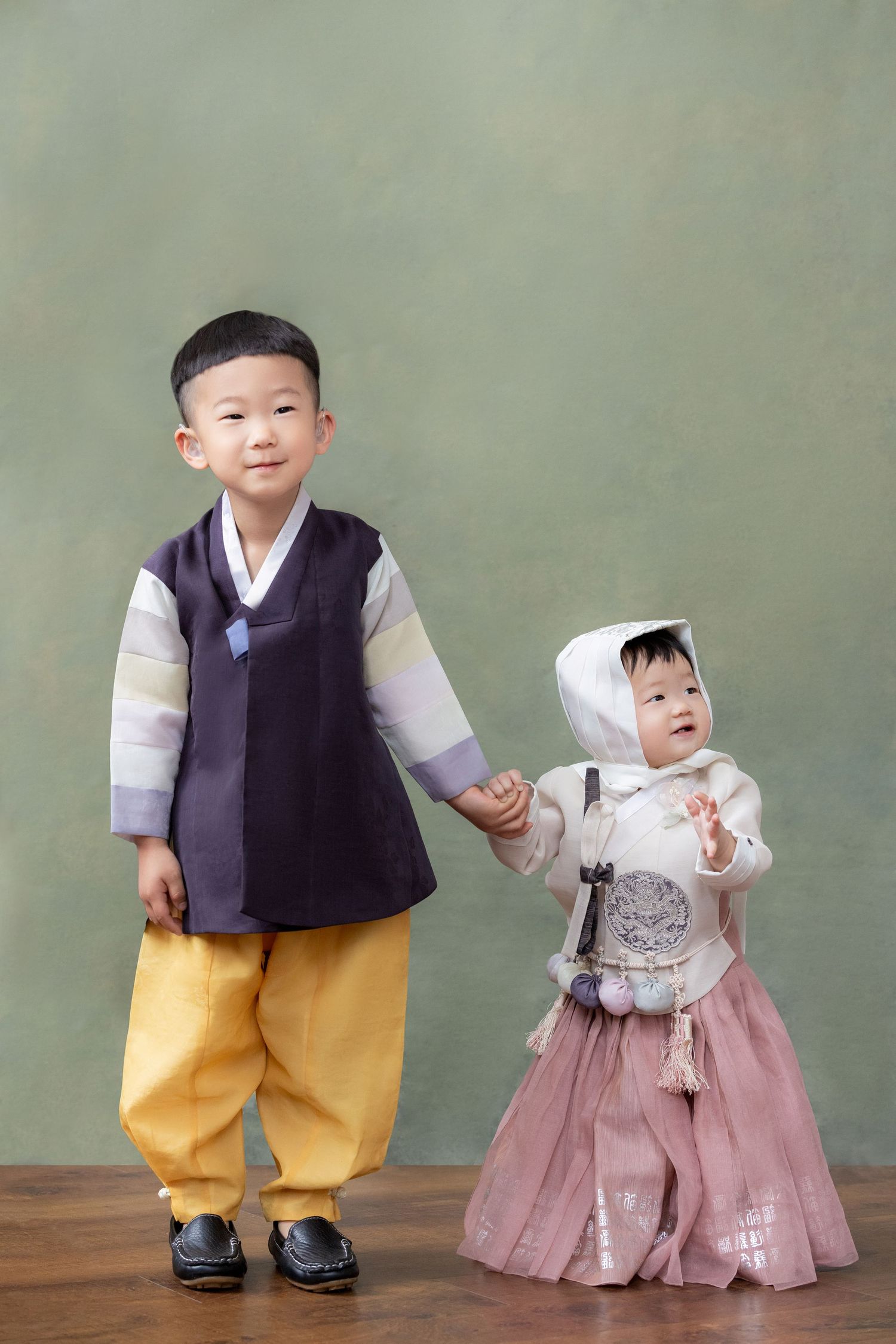 Two young children wearing traditional Korean hanbok outfits posing together against a green background.