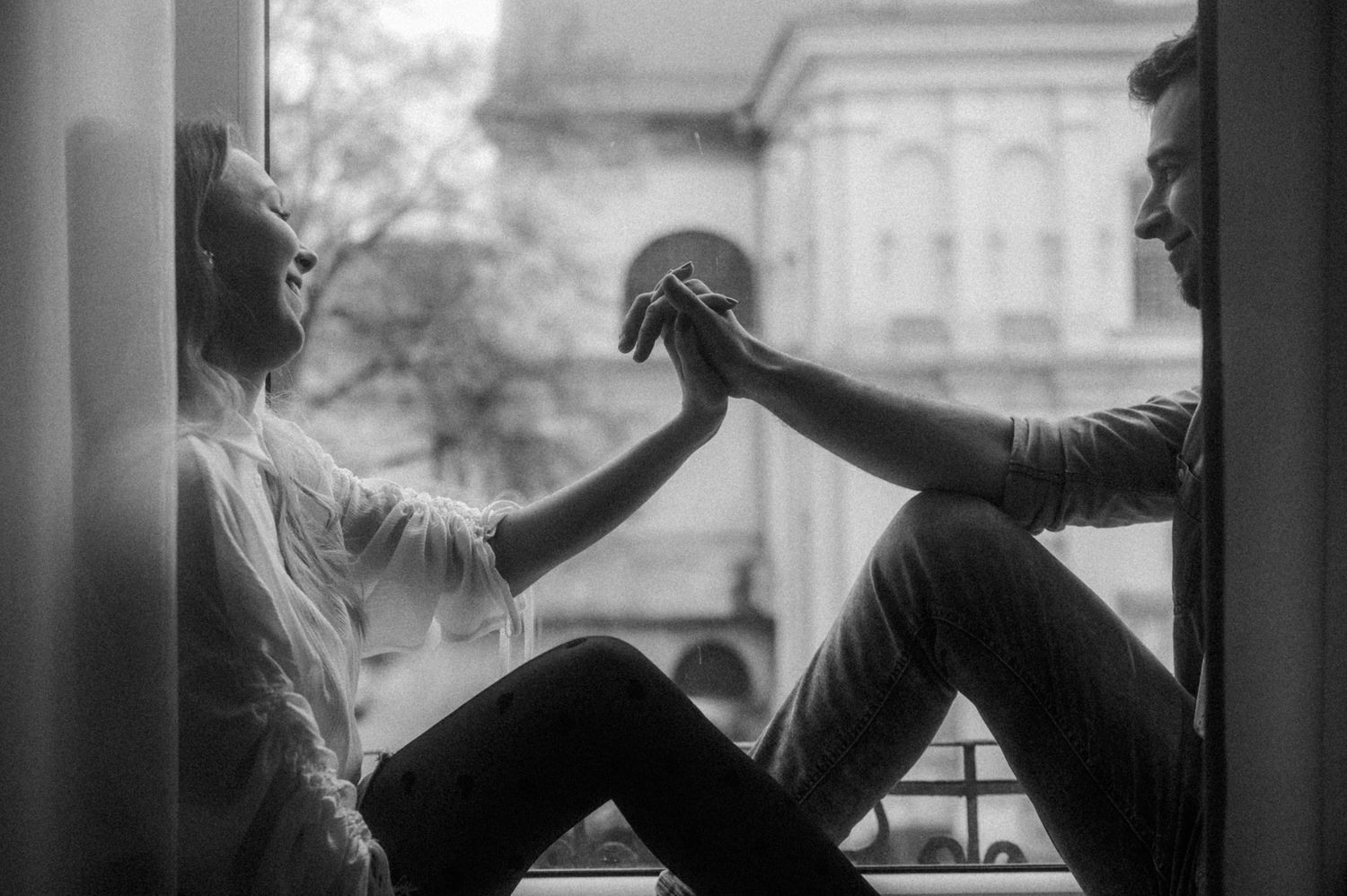 Black and white photo showing silhouettes of people dancing with their hands raised against a bright window backdrop.