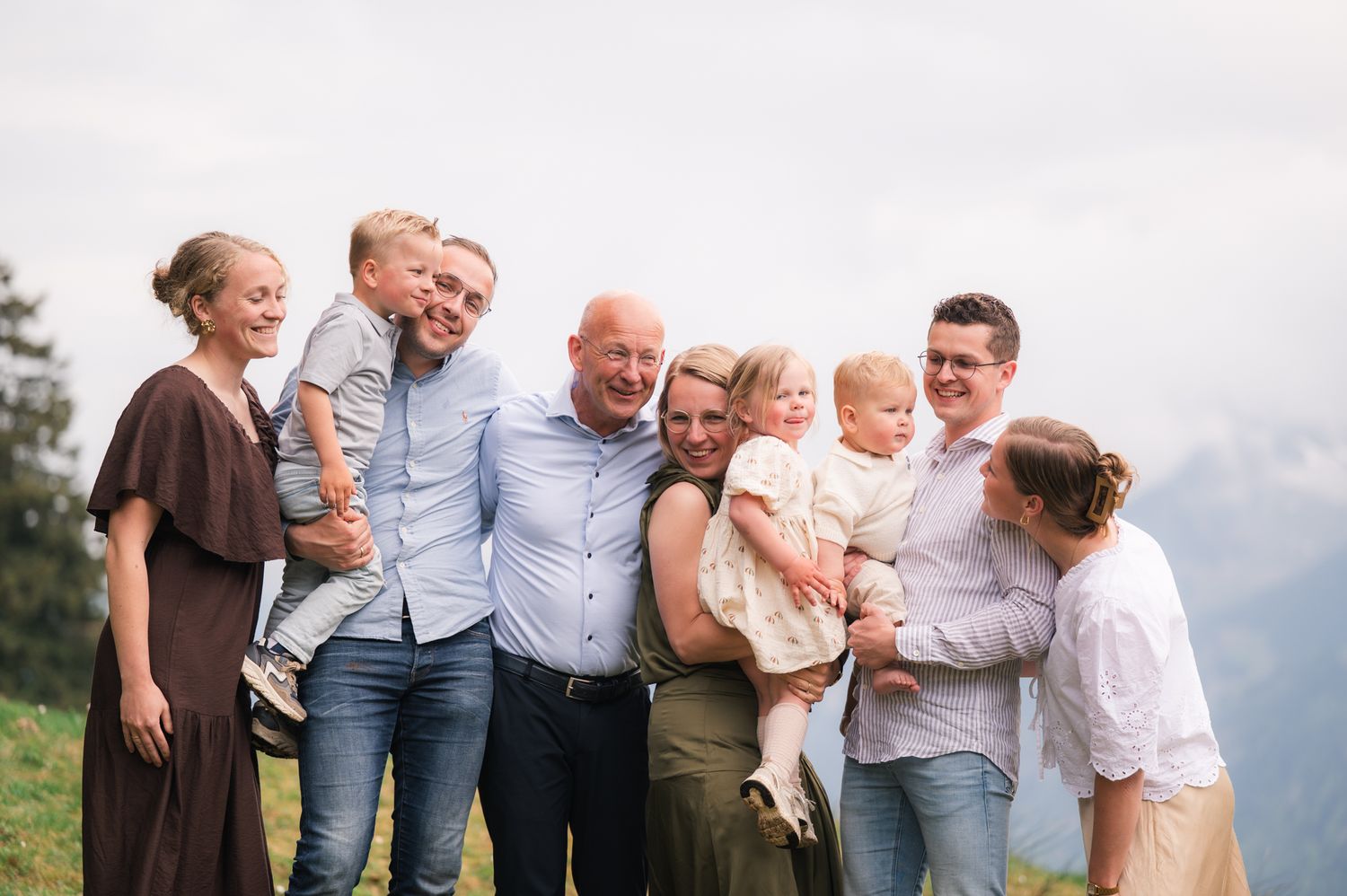 Large family group smiling together outdoors on a mountain overlook on a cloudy day.