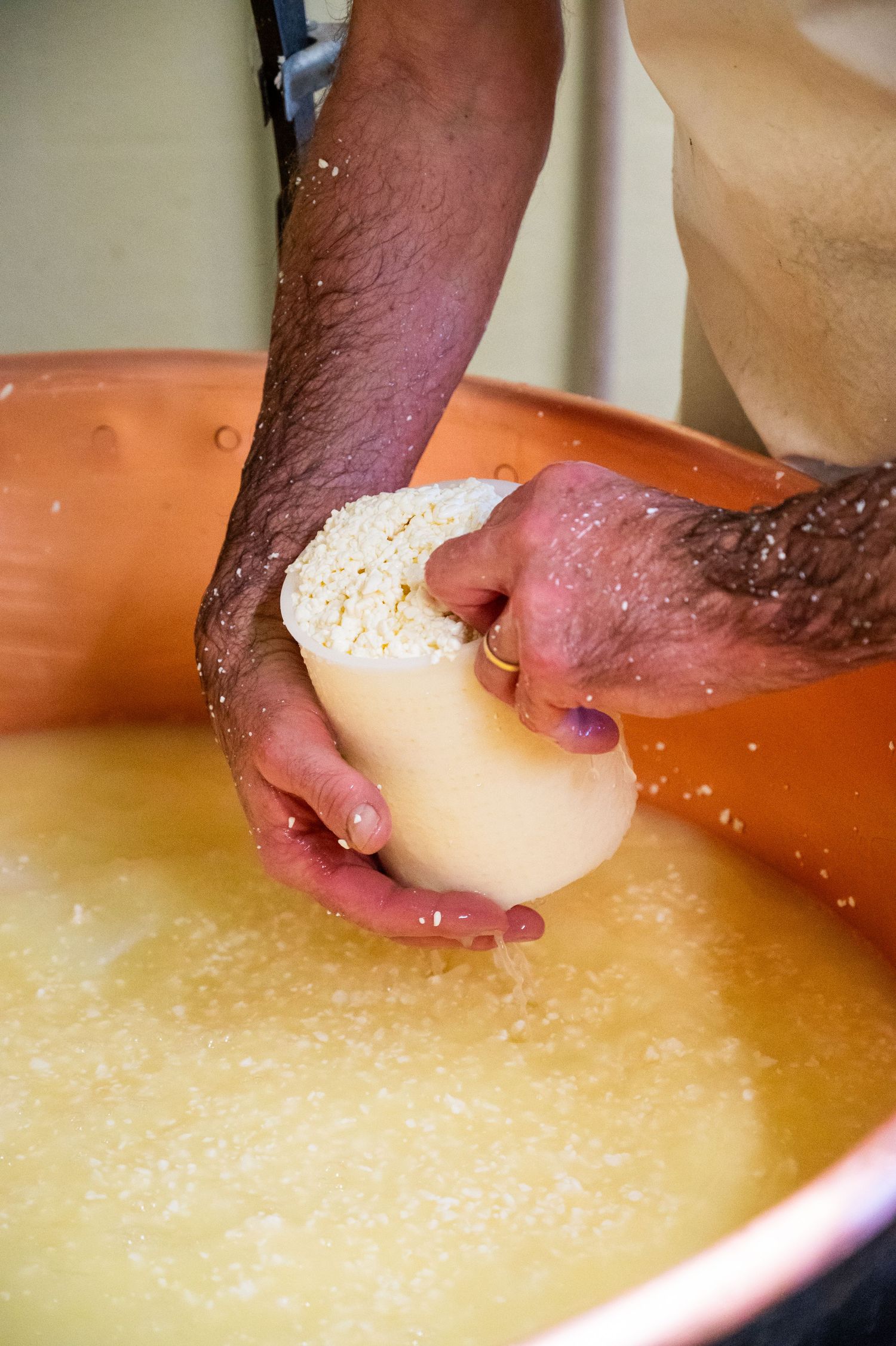 Hands kneading fresh dough on a floured surface in a terracotta bowl during bread making preparation.