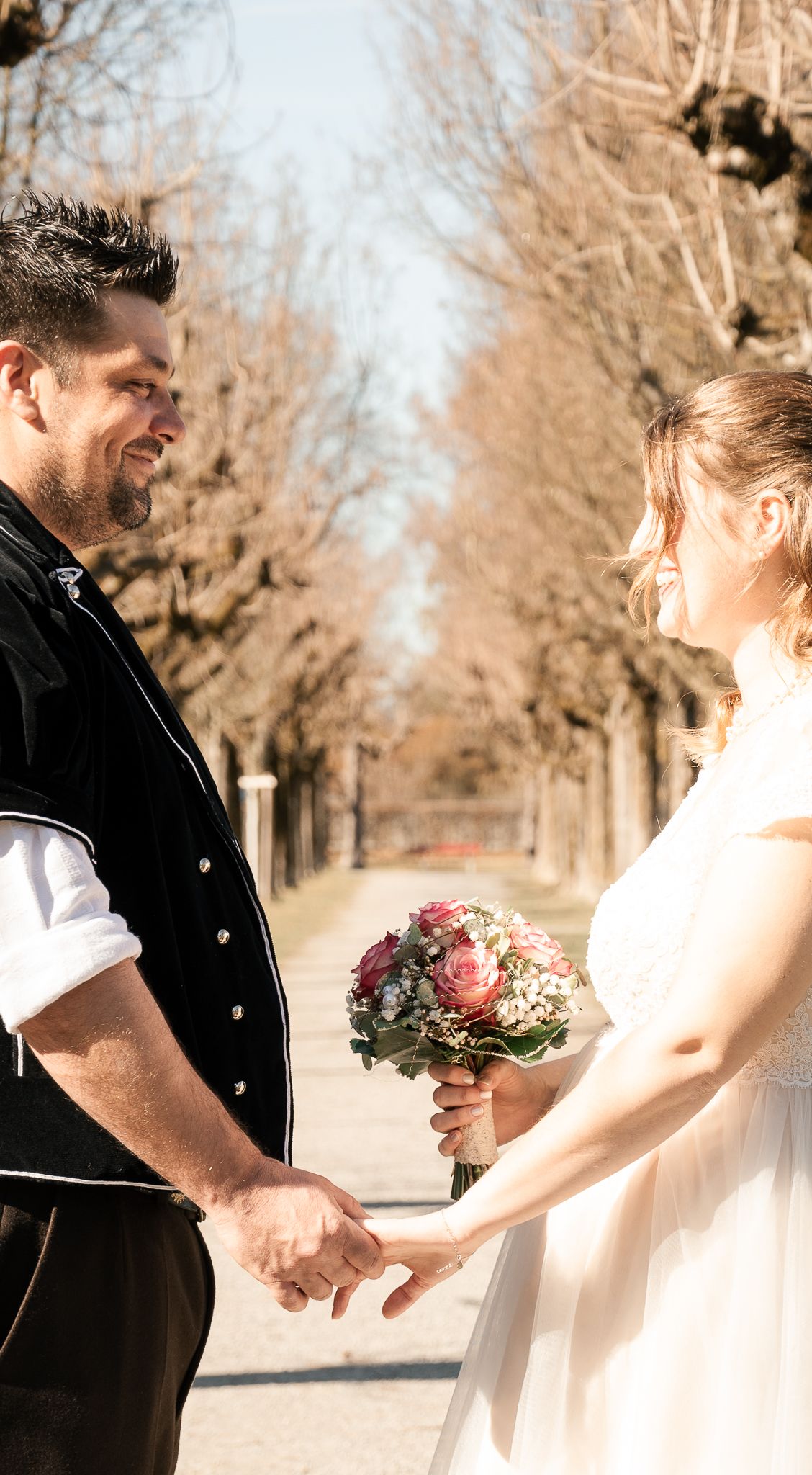 A romantic winter wedding scene shows a couple in formal attire holding hands on a tree-lined path.
