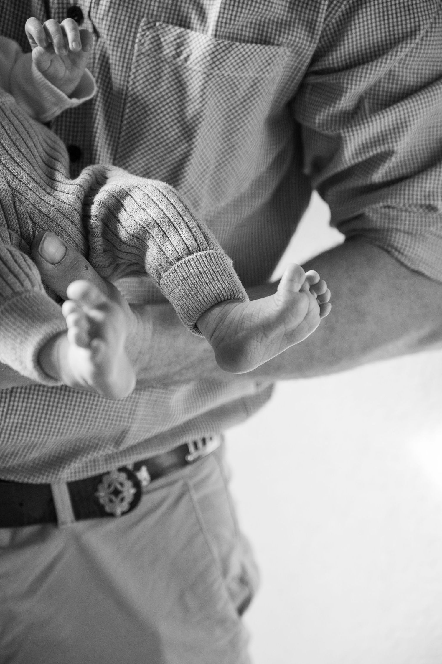 Black and white close-up of tiny baby feet being held in adult hands.