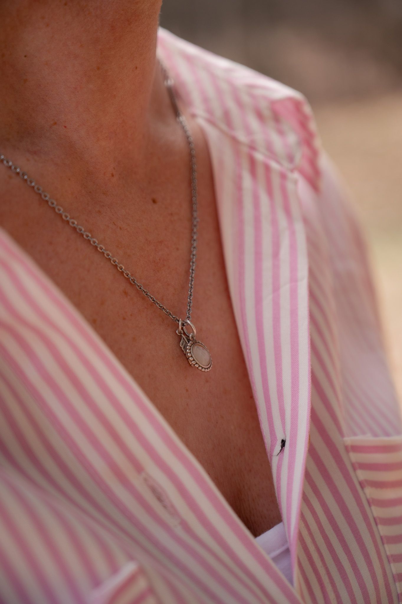 Close-up sequence showing a delicate silver necklace with heart pendant against a pink and white striped shirt.