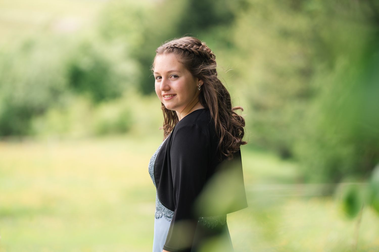 Young woman with braided hair smiling over her shoulder outdoors in a lush green garden setting.