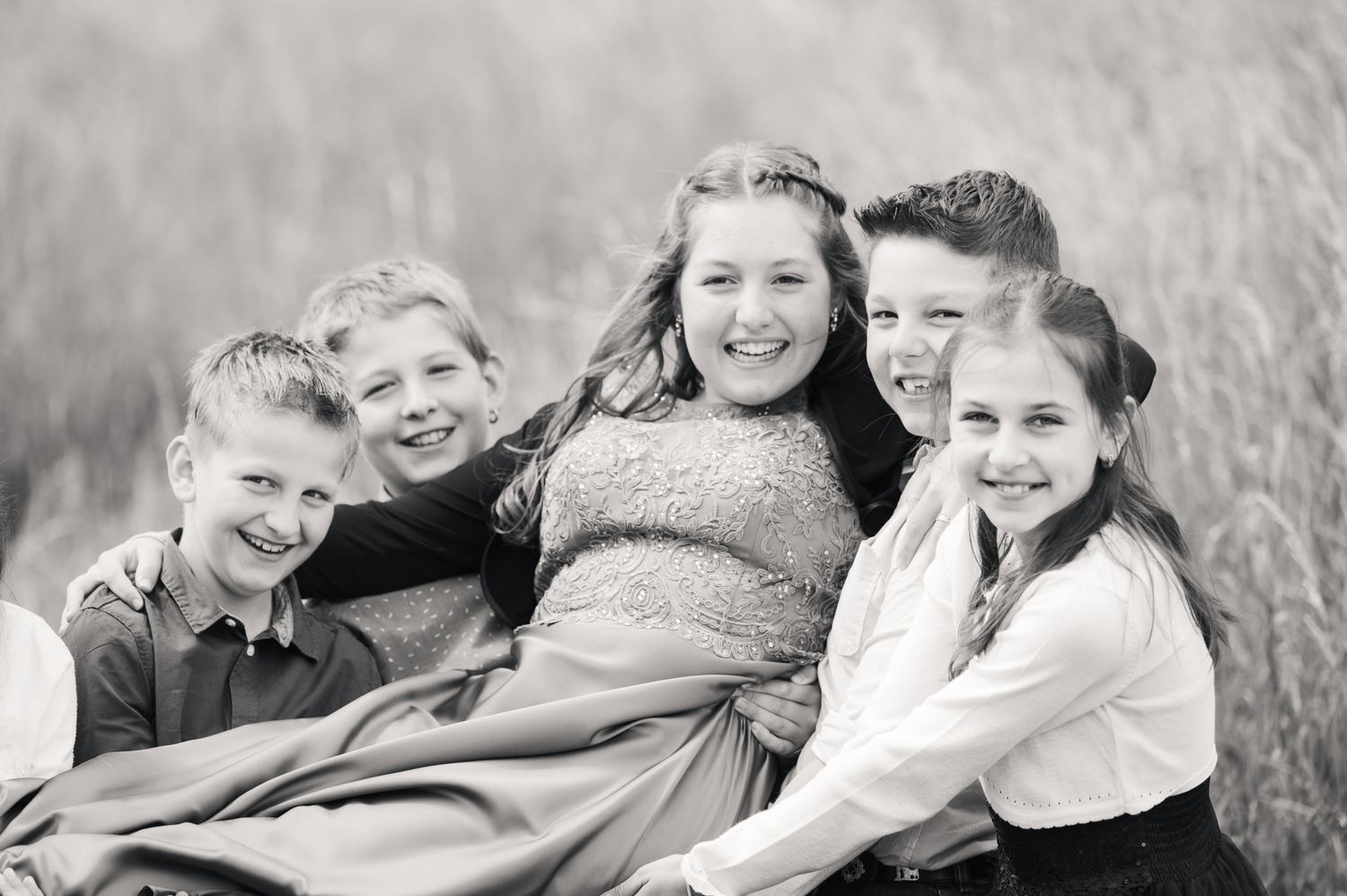Black and white photo of five smiling children sitting together in a grassy field.