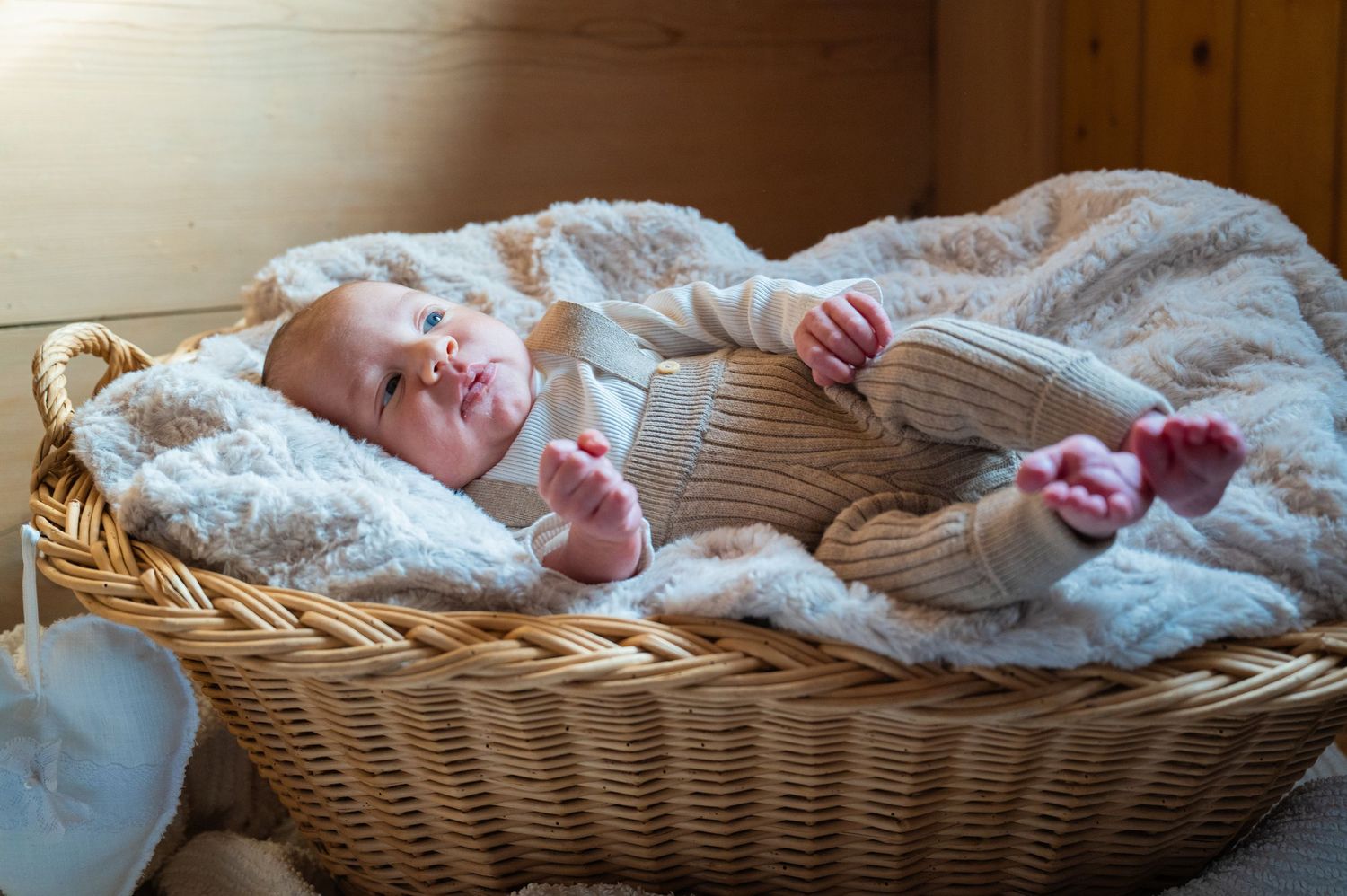 Newborn baby sleeping peacefully in white blankets in wicker basket.