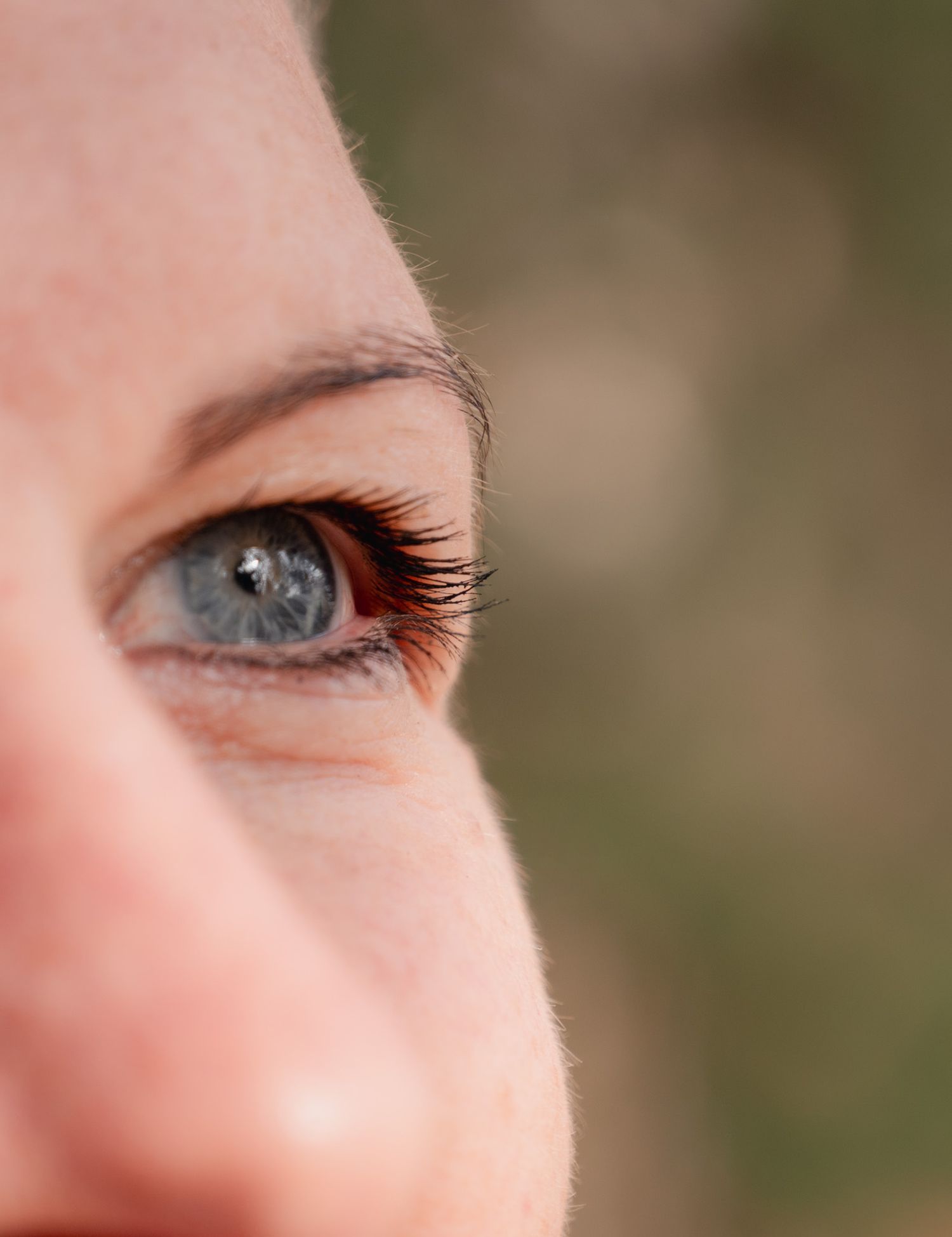 Close-up macro shot of a blue human eye with long eyelashes against a blurred natural background.