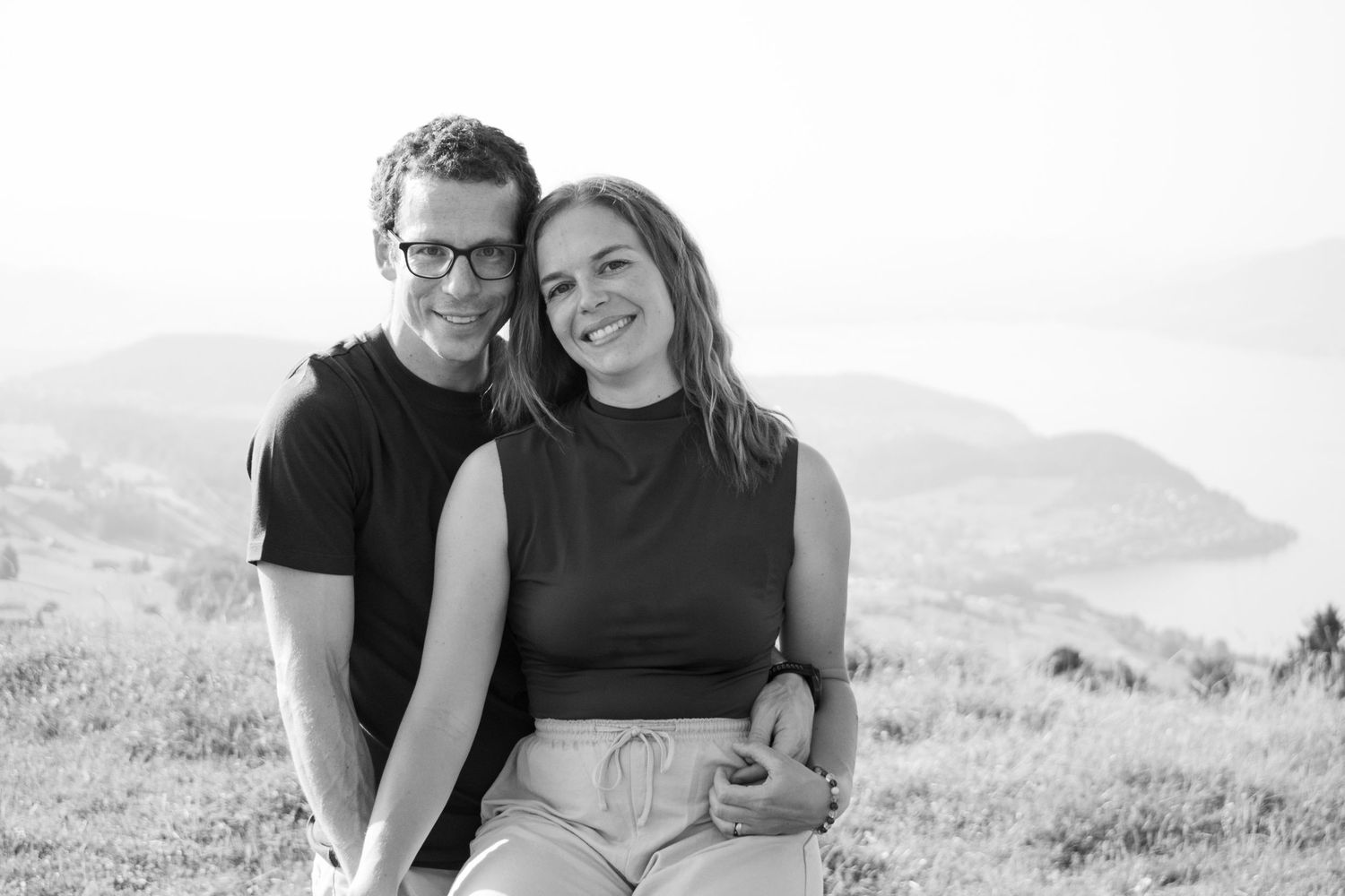 Couple embracing on a hillside overlooking a scenic mountain landscape.
